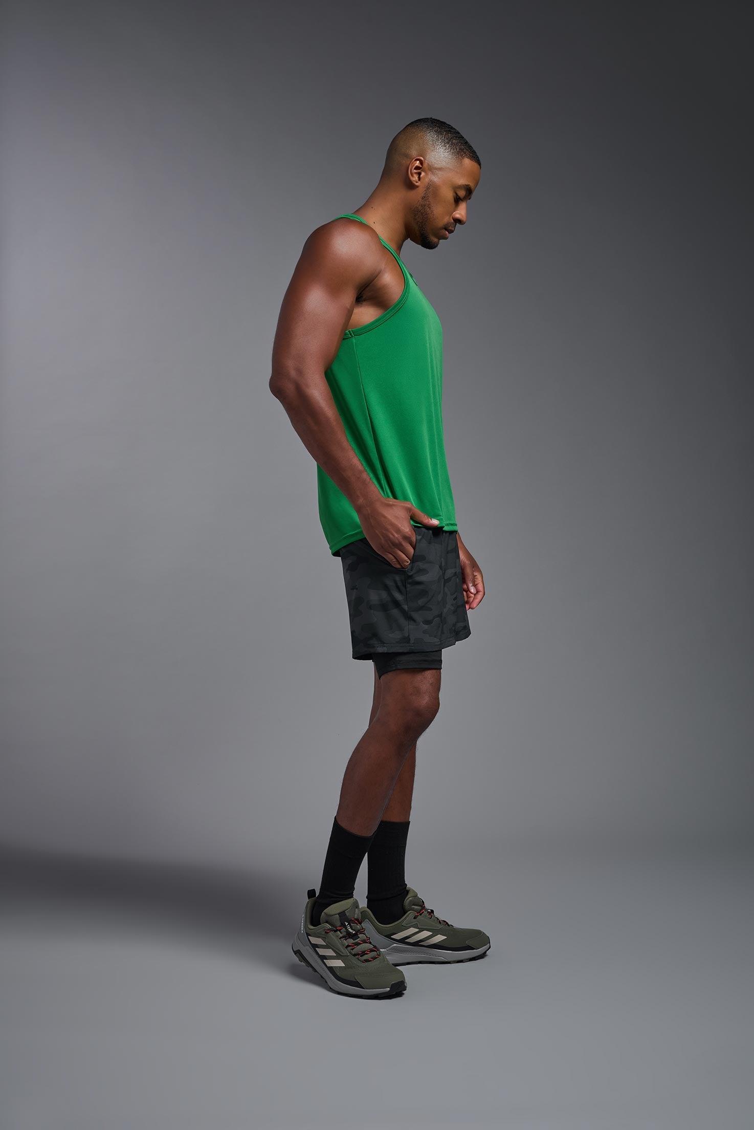 A male model wearing the men's DriMax Endurance Tank in the color kelly green, made out of 100% polyester, showing the relaxed fit from a side view. #kelly