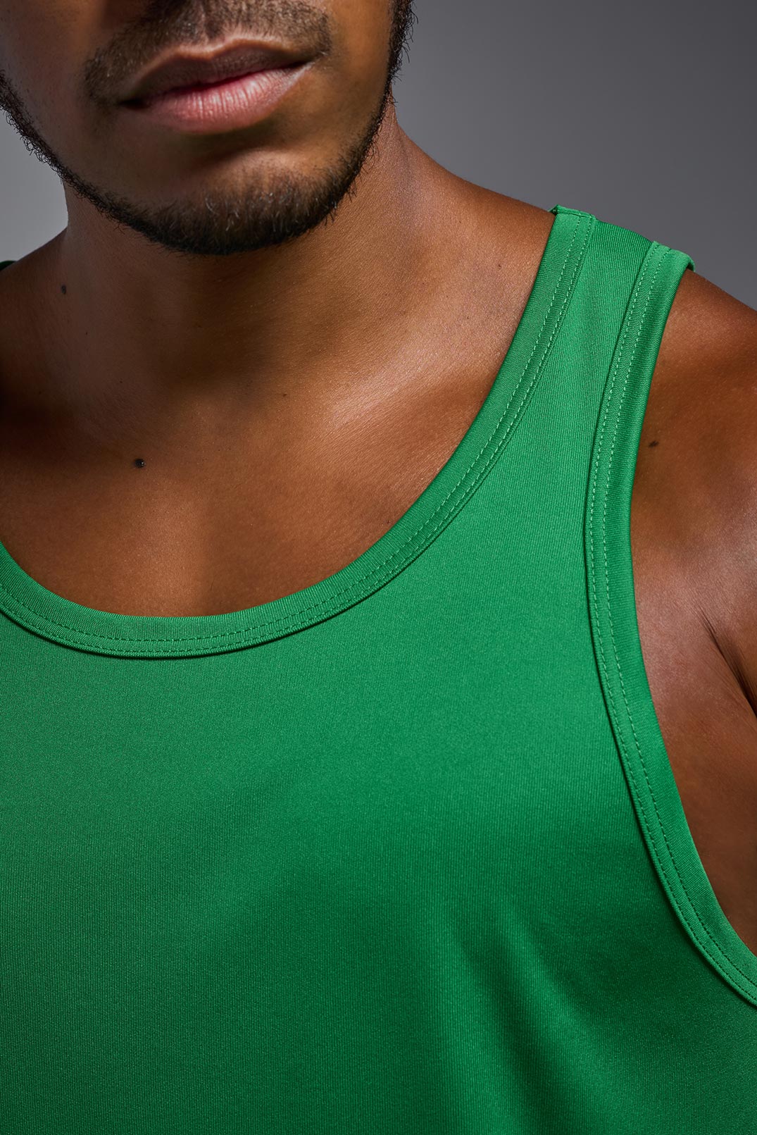 A male model wearing the men's DriMax Endurance Tank in the color kelly green, made out of 100% polyester, showing the relaxed fit from a close-up collar view. #kelly