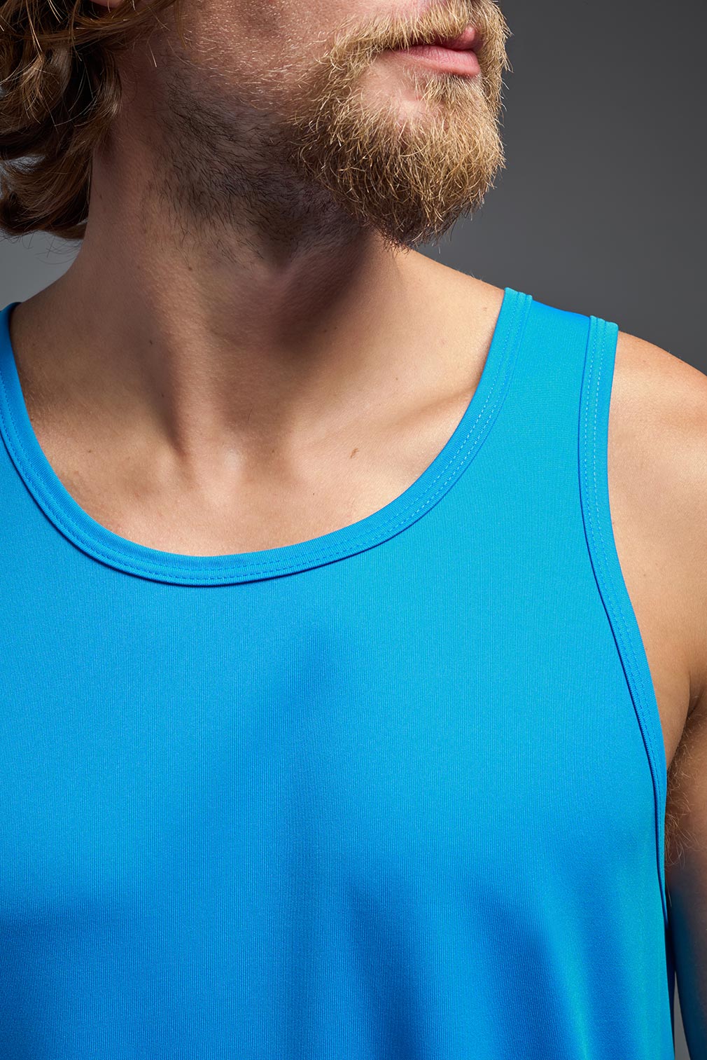 A male model wearing the men's DriMax Endurance Tank in the color safety blue, made out of 100% polyester, showing the relaxed fit from a close-up collar view. This tank is quick-drying and moisture-wicking and made in the USA #safety-blue