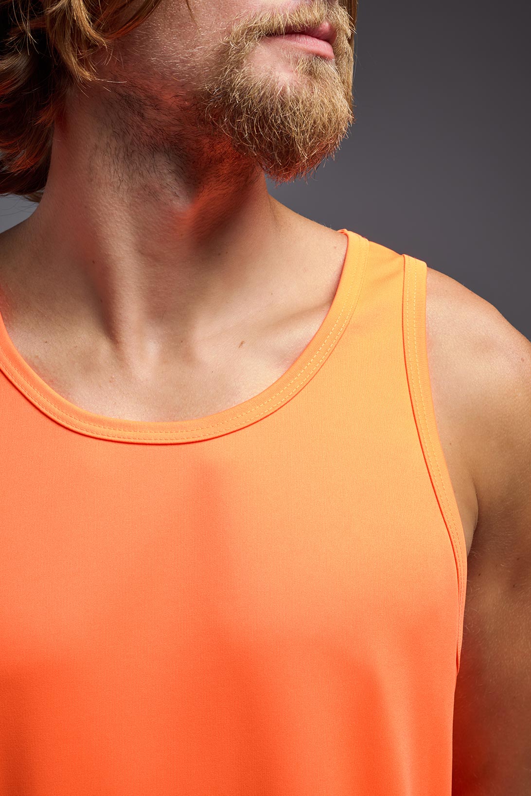 A male model wearing the men's DriMax Endurance Tank in the color safety orange, made out of 100% polyester, showing the relaxed fit from a collar view. #safety-orange