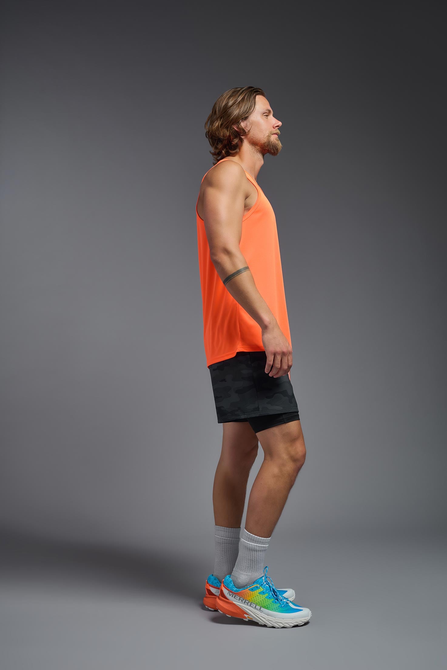 A male model wearing the men's DriMax Endurance Tank in the color safety orange, made out of 100% polyester, showing the relaxed fit from a side view. #safety-orange