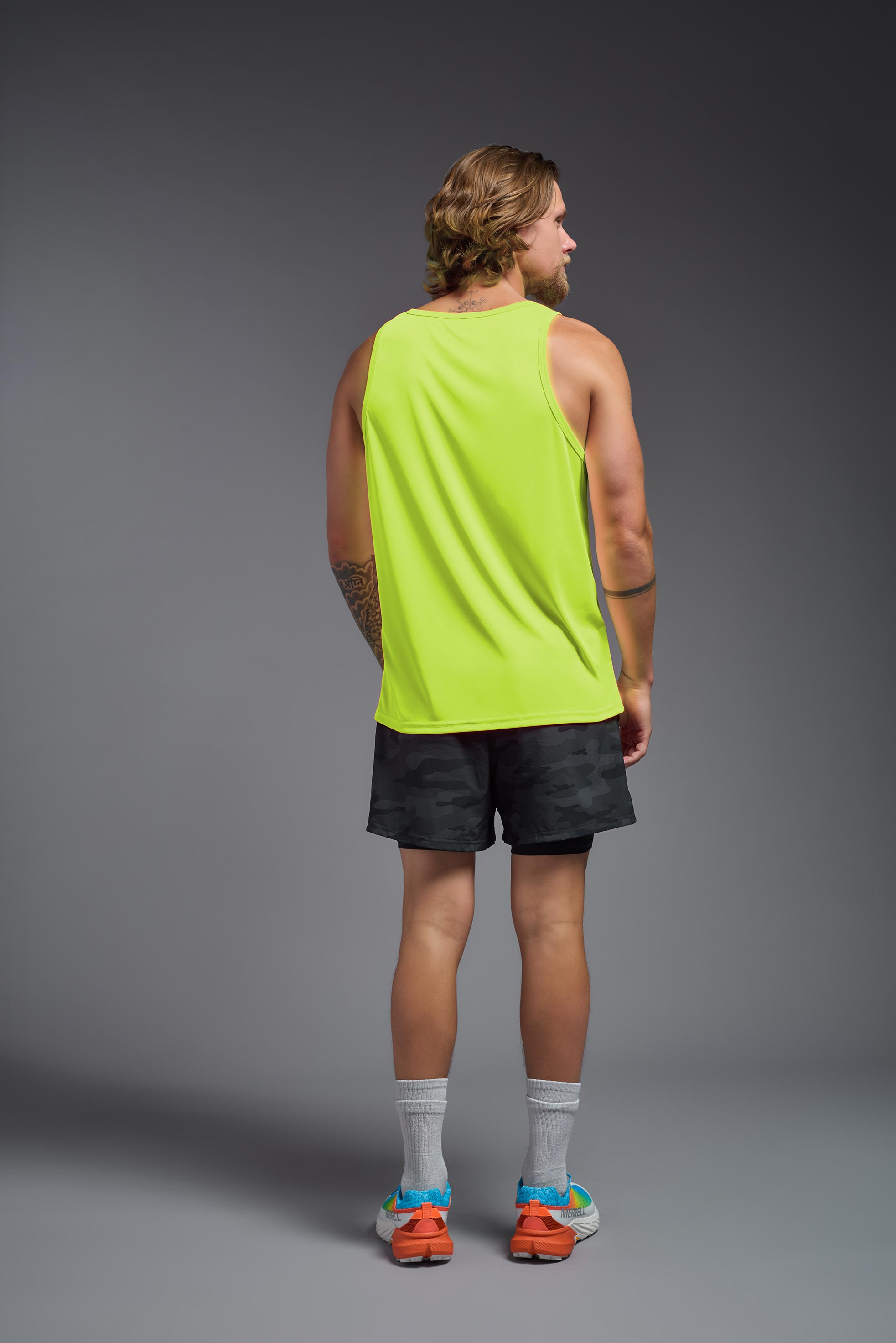 A male model wearing the men's DriMax Endurance Tank in the color safety yellow, made out of 100% polyester, showing the relaxed fit from a back view. This tank is quick-drying and moisture-wicking and made in the USA #safety-yellow