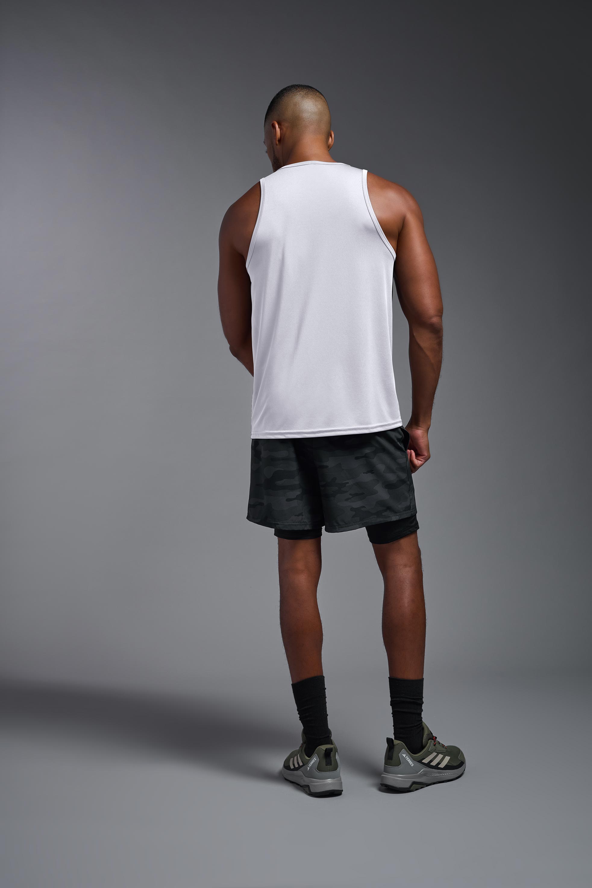 A male model wearing the men's DriMax Endurance Tank in the color white, made out of 100% polyester, showing the relaxed fit from a back view. This tank is quick-drying and moisture-wicking and made in the USA #white