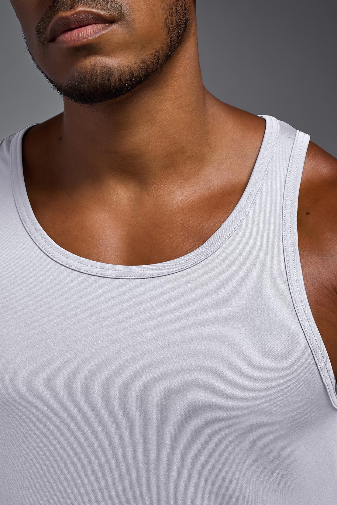 A male model wearing the men's DriMax Endurance Tank in the color white, made out of 100% polyester, showing the relaxed fit from a closeup collar front view. This tank is quick-drying and moisture-wicking and made in the USA #white