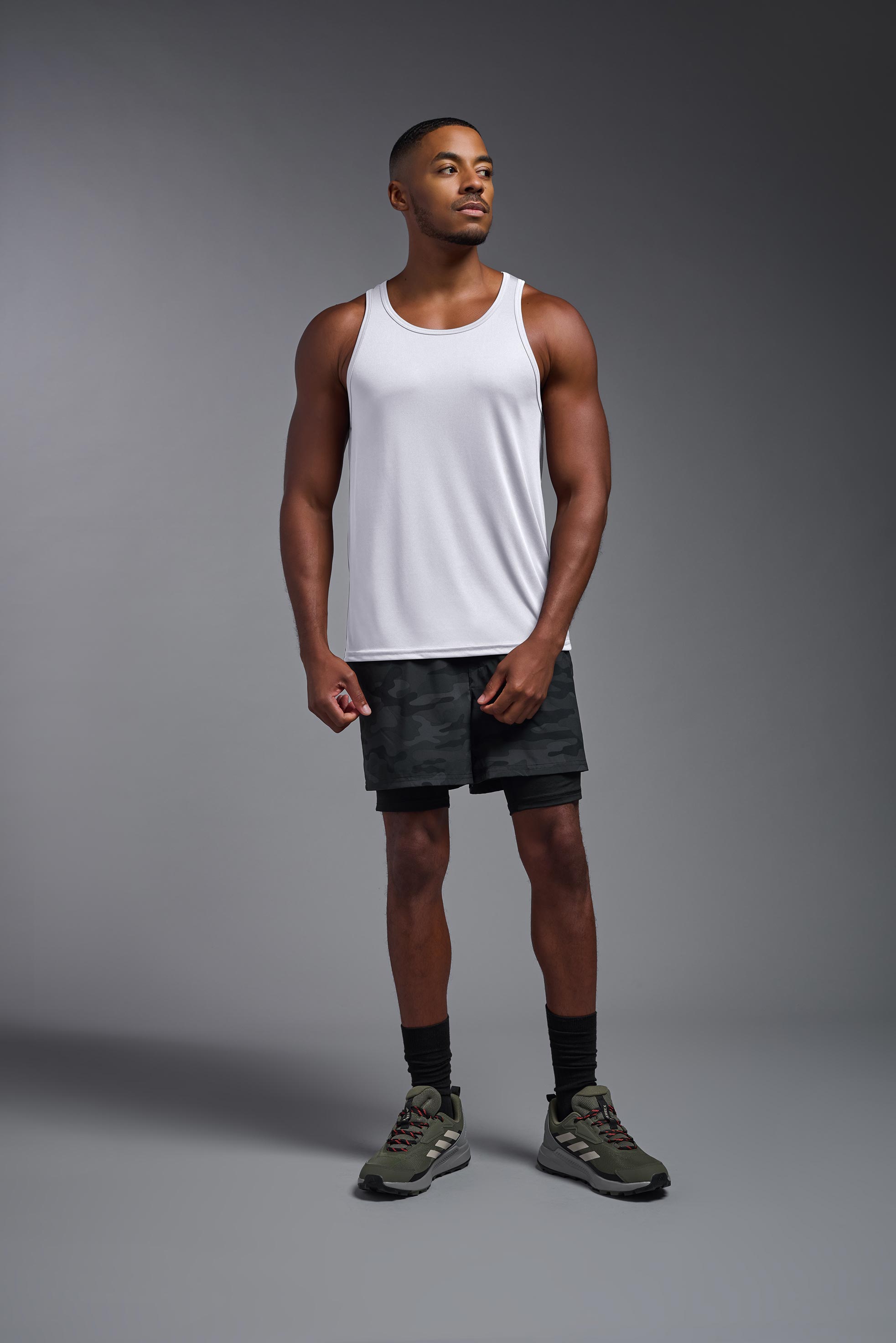 A male model wearing the men's DriMax Endurance Tank in the color white, made out of 100% polyester, showing the relaxed fit from a front view. This tank is quick-drying and moisture-wicking and made in the USA #white