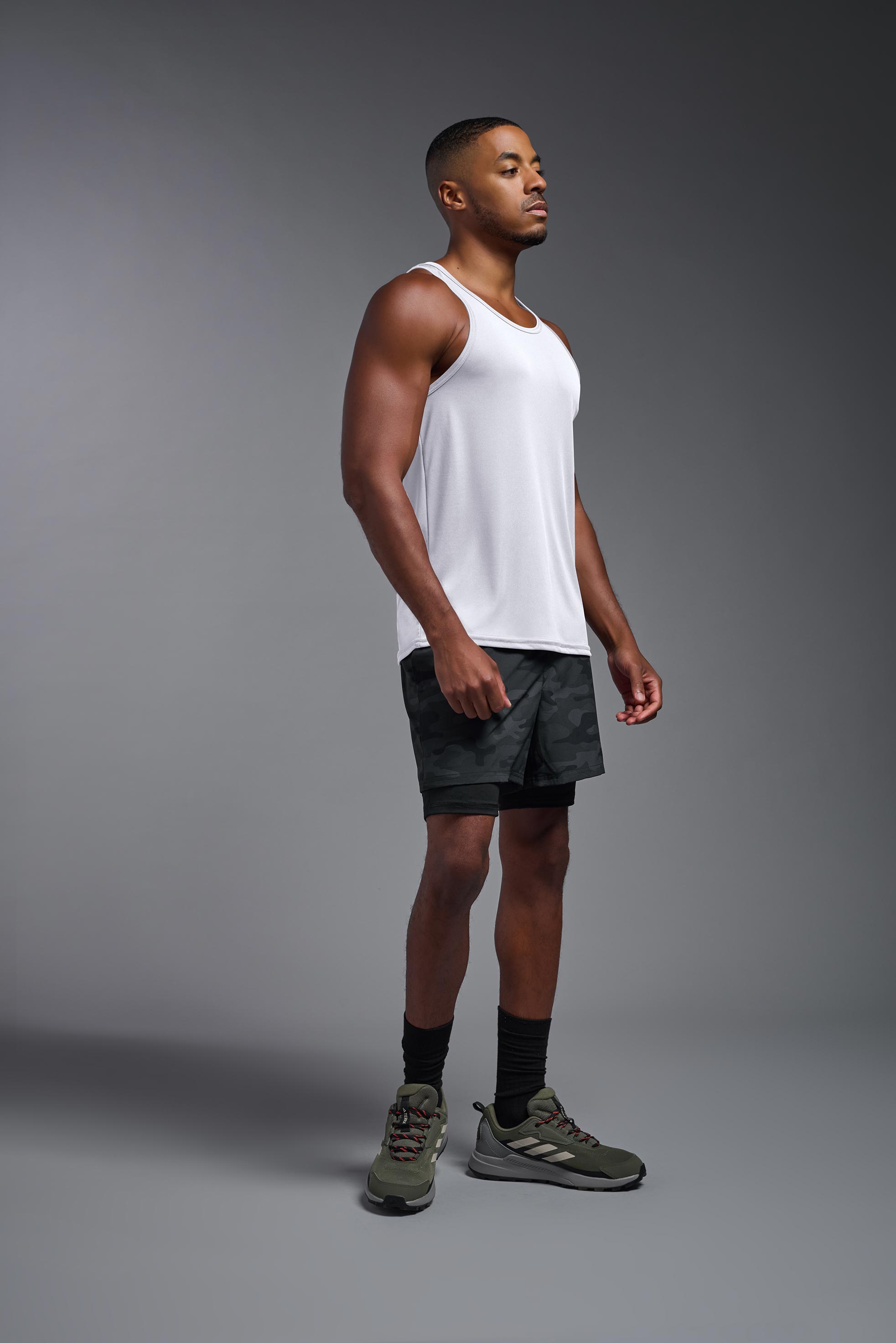 A male model wearing the men's DriMax Endurance Tank in the color white, made out of 100% polyester, showing the relaxed fit from a side view. This tank is quick-drying and moisture-wicking and made in the USA #white