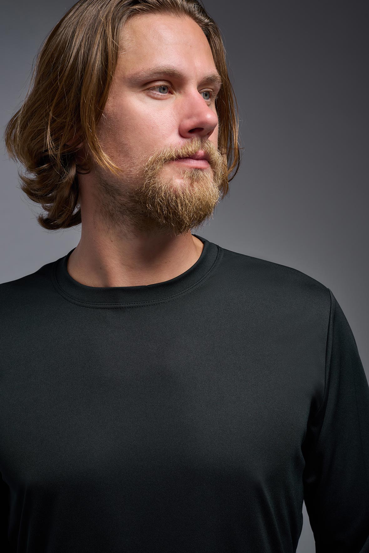 A male model wearing the men's DriMax Long Sleeve Expert Tee in black, made out of 100% polyester, showing the relaxed fit from a detail collar view. #black