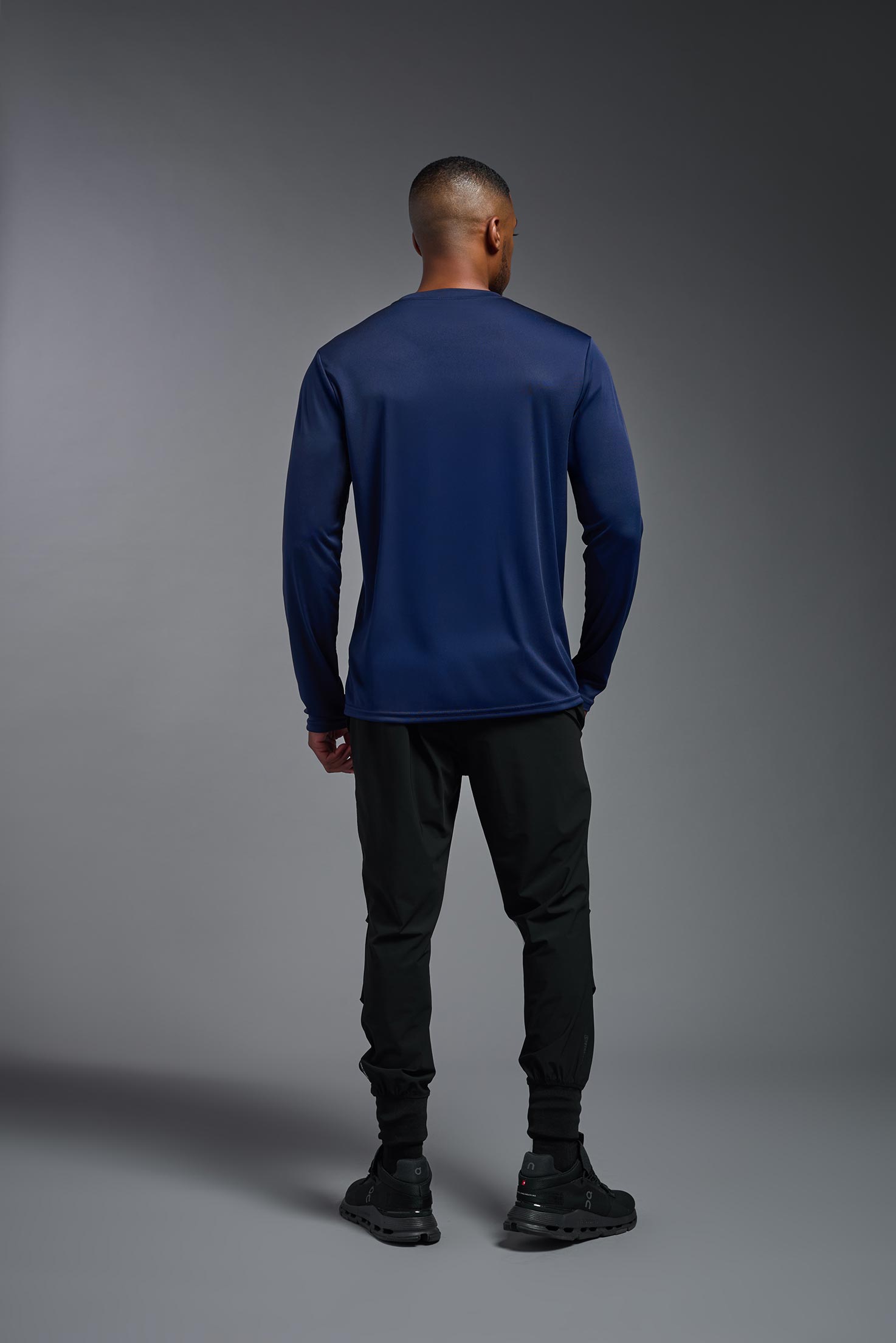 A male model wearing the men's DriMax Long Sleeve Expert Tee in the color navy blue, made out of 100% polyester, showing the relaxed fit from a back view. #navy