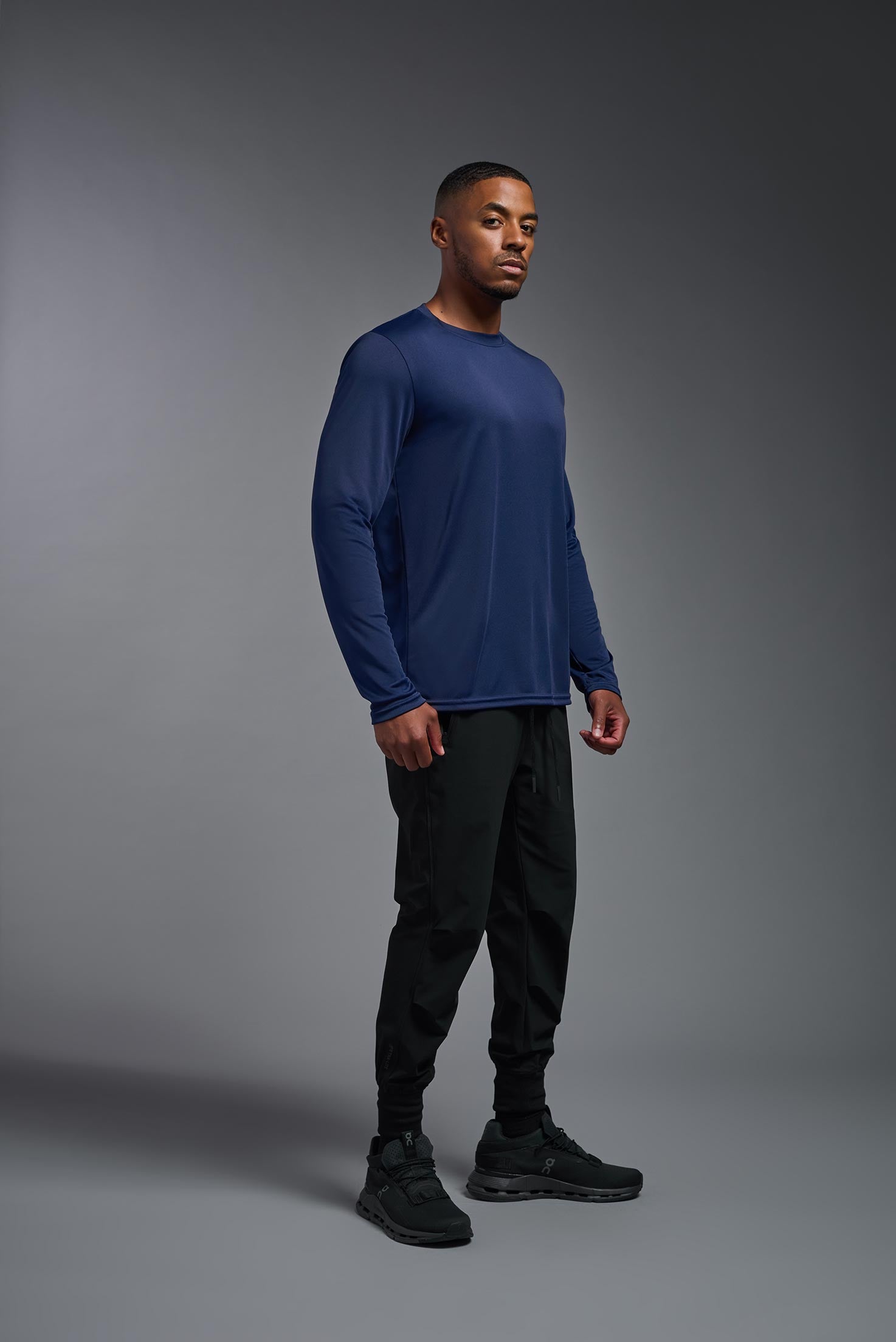 A male model wearing the men's DriMax Long Sleeve Expert Tee in the color navy blue, made out of 100% polyester, showing the relaxed fit from a sideview. #navy
