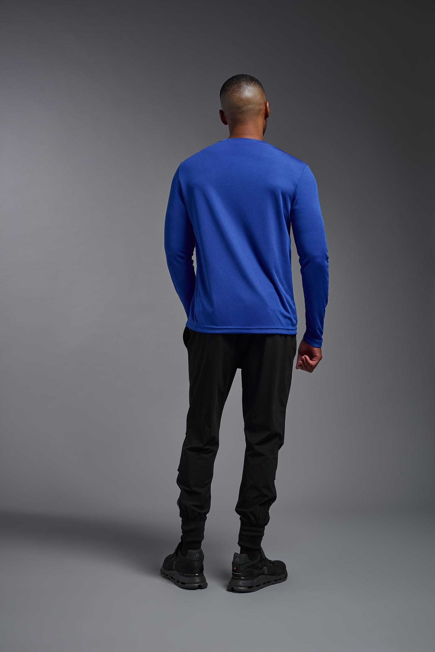 A male model wearing the men's DriMax Long Sleeve Expert Tee in the color royal blue, made out of 100% polyester, showing the relaxed fit from a back view. #royal