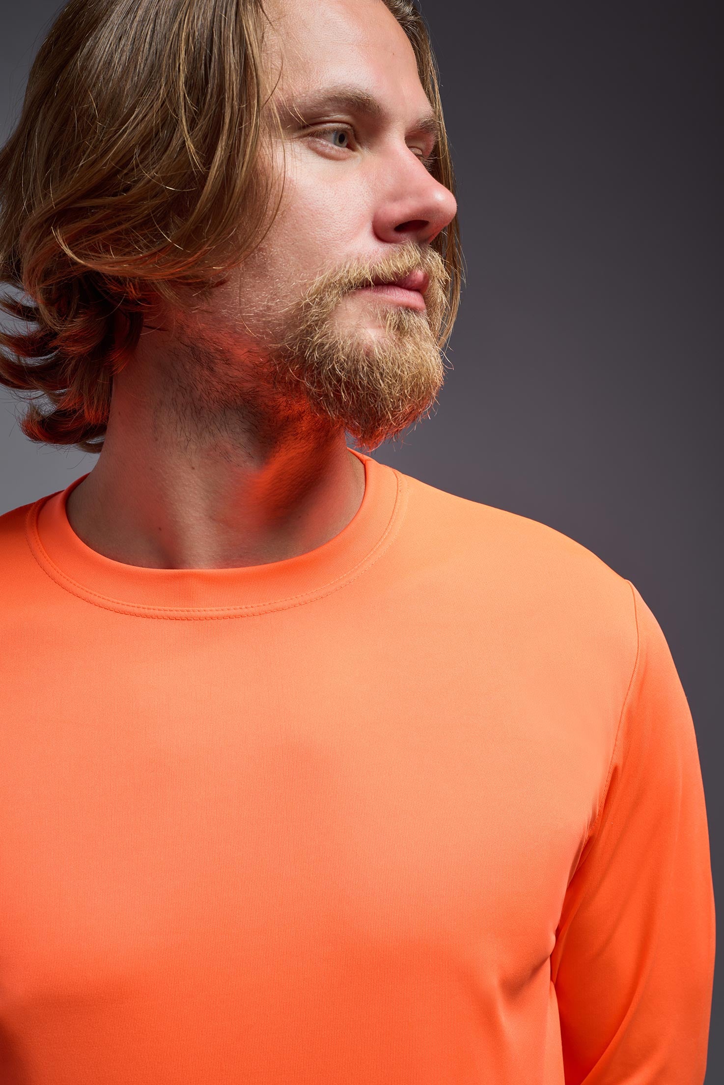 A male model wearing the men's DriMax Long Sleeve Expert Tee in the color safety orange, made out of 100% polyester, showing the relaxed fit from a collar detail view. #safety-orange