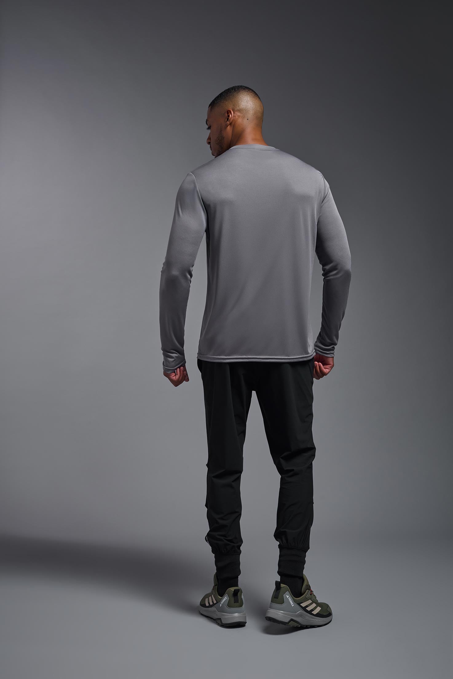 A male model wearing the men's DriMax Long Sleeve Expert Tee in the color steel, made out of 100% polyester, showing the relaxed fit from a back view. #steel