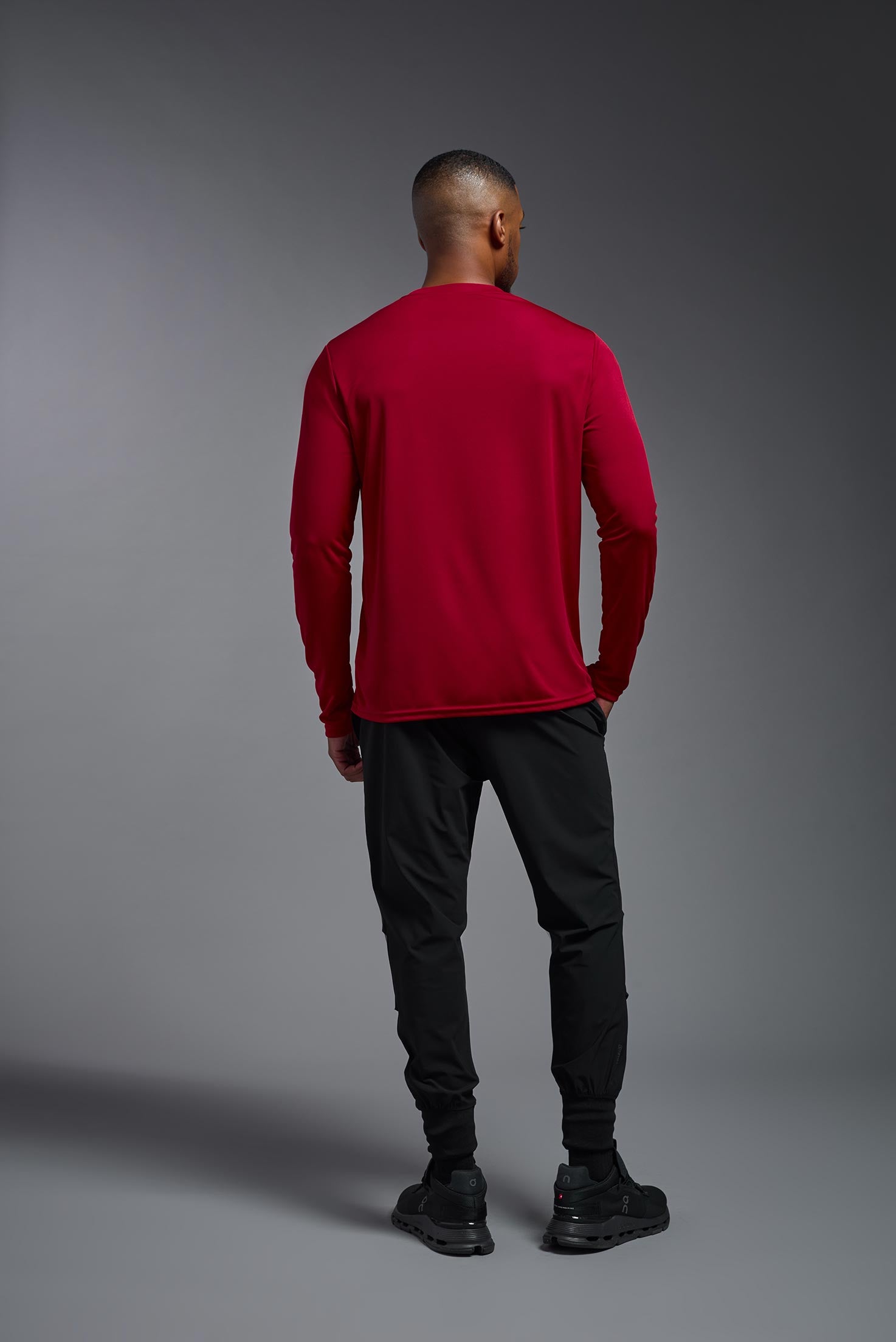 A male model wearing the men's DriMax Long Sleeve Expert Tee in red, made out of 100% polyester, showing the relaxed fit from a back view. #red