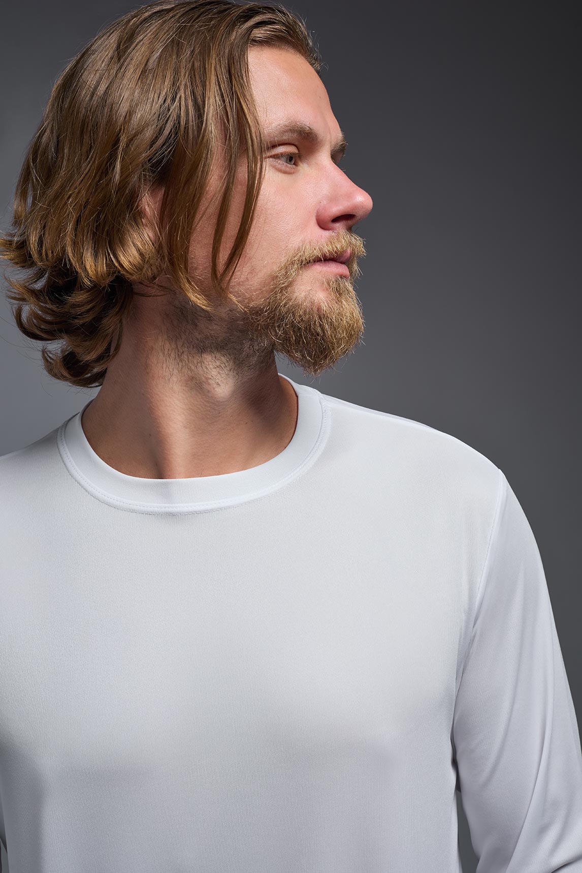 A male model wearing the men's DriMax Long Sleeve Expert Tee in the color white, made out of 100% polyester, showing the relaxed fit from a detail collar view. #white