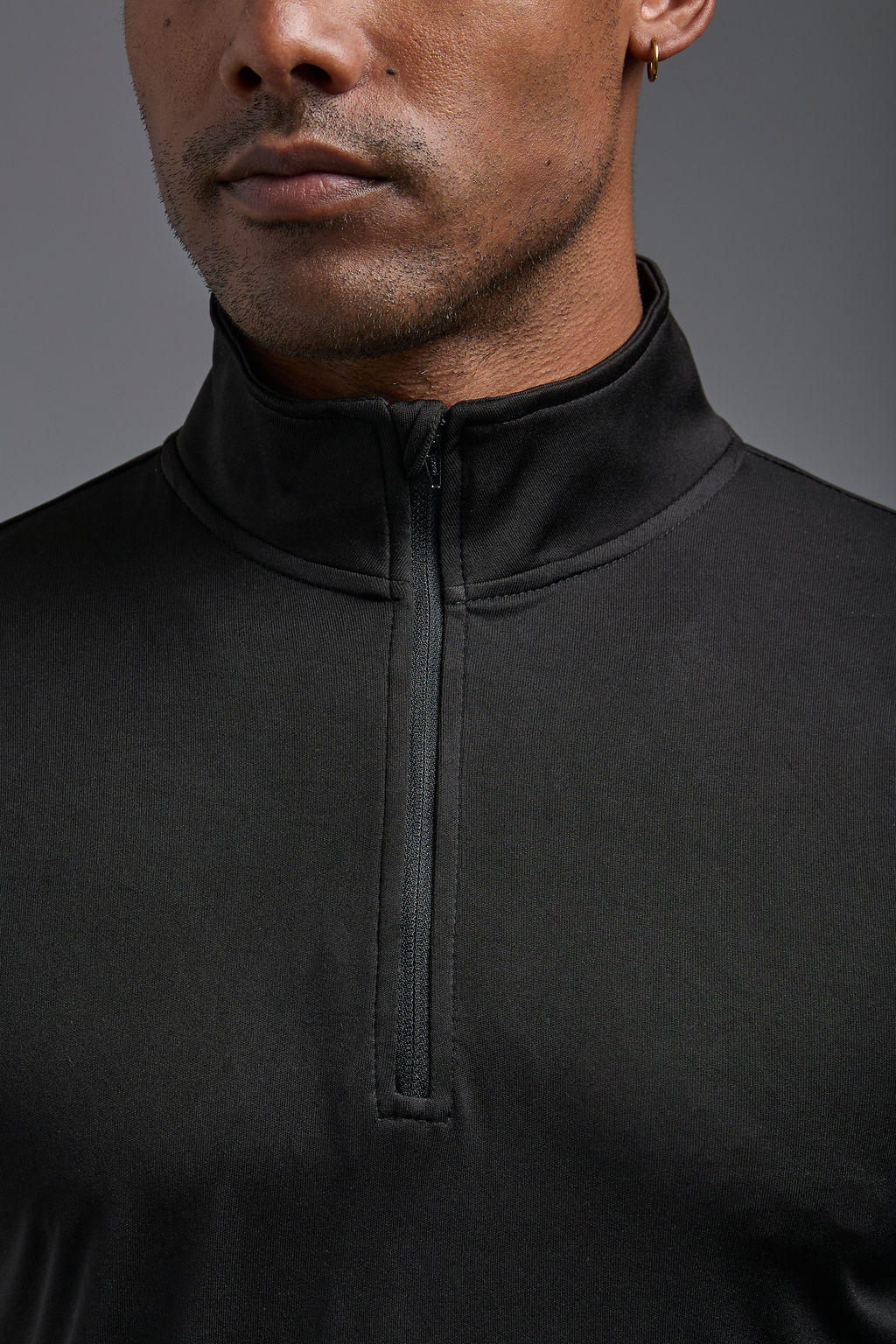 A male model wearing the men's DriMax Quarterzip Training Top in the color black, made out of 100% polyester, showing the relaxed fit from a front close up collar view. This Quarter Zip is made in the USA wicks sweat, quick dries like drifit, and controls odors. #black