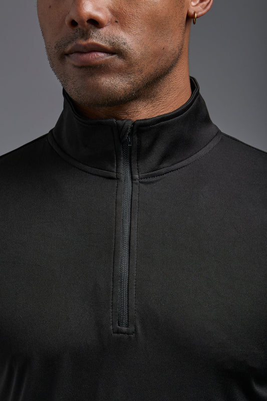 A male model wearing the men's DriMax Quarterzip Training Top in the color black, made out of 100% polyester, showing the relaxed fit from a front close up collar view. This Quarter Zip is made in the USA wicks sweat, quick dries like drifit, and controls odors. #black