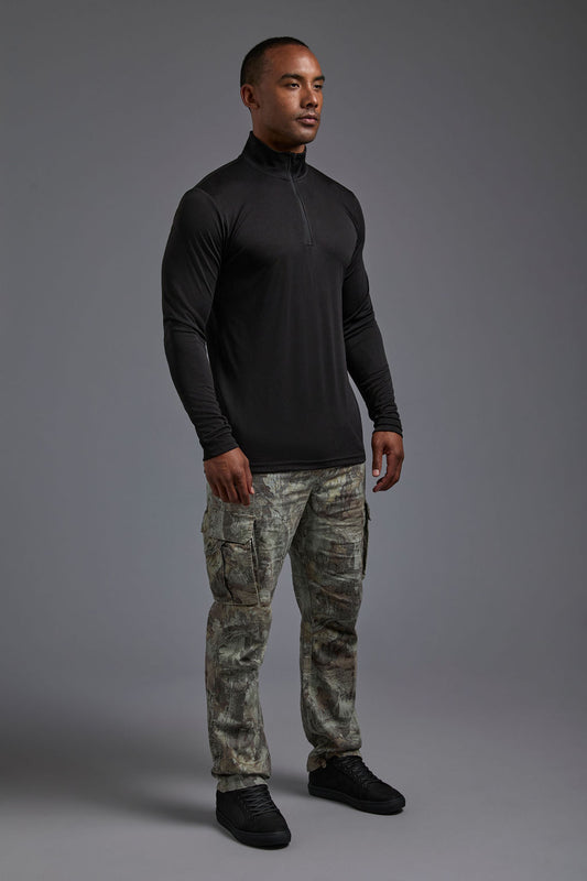 A male model wearing the men's DriMax Quarterzip Training Top in the color black, made out of 100% polyester, showing the relaxed fit from a side view. This Quarter Zip is made in the USA wicks sweat, quick dries like drifit, and controls odors. #black