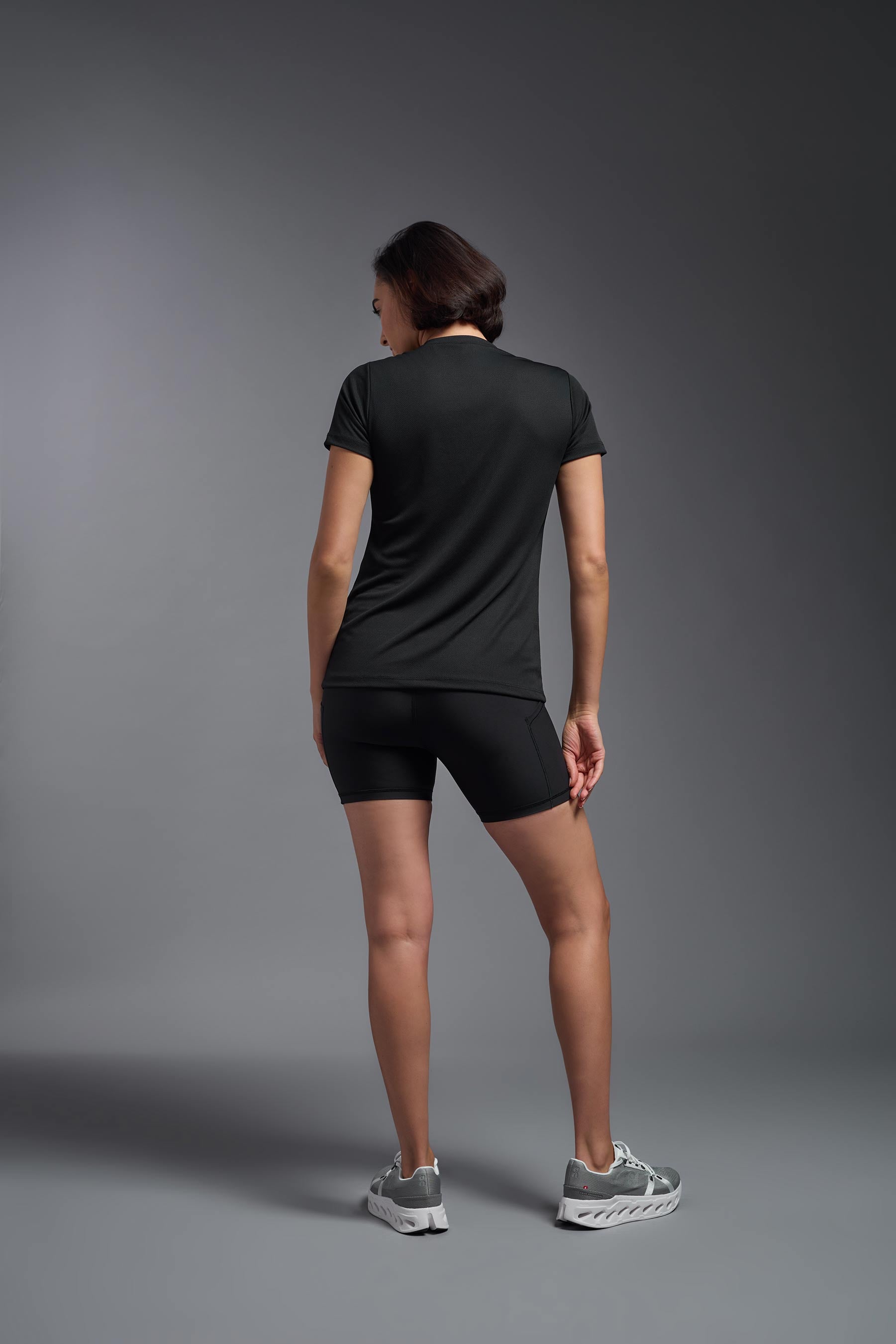 A female model wearing the women's Oxymesh V-neck Tech Tee Imported Version in the color black, made out of 100% polyester, showing the relaxed fit from a close-up collar back view. This shirt is breathable, quick-drying, moisture-wicking, and Imported for a better price on bulk apparel. #black