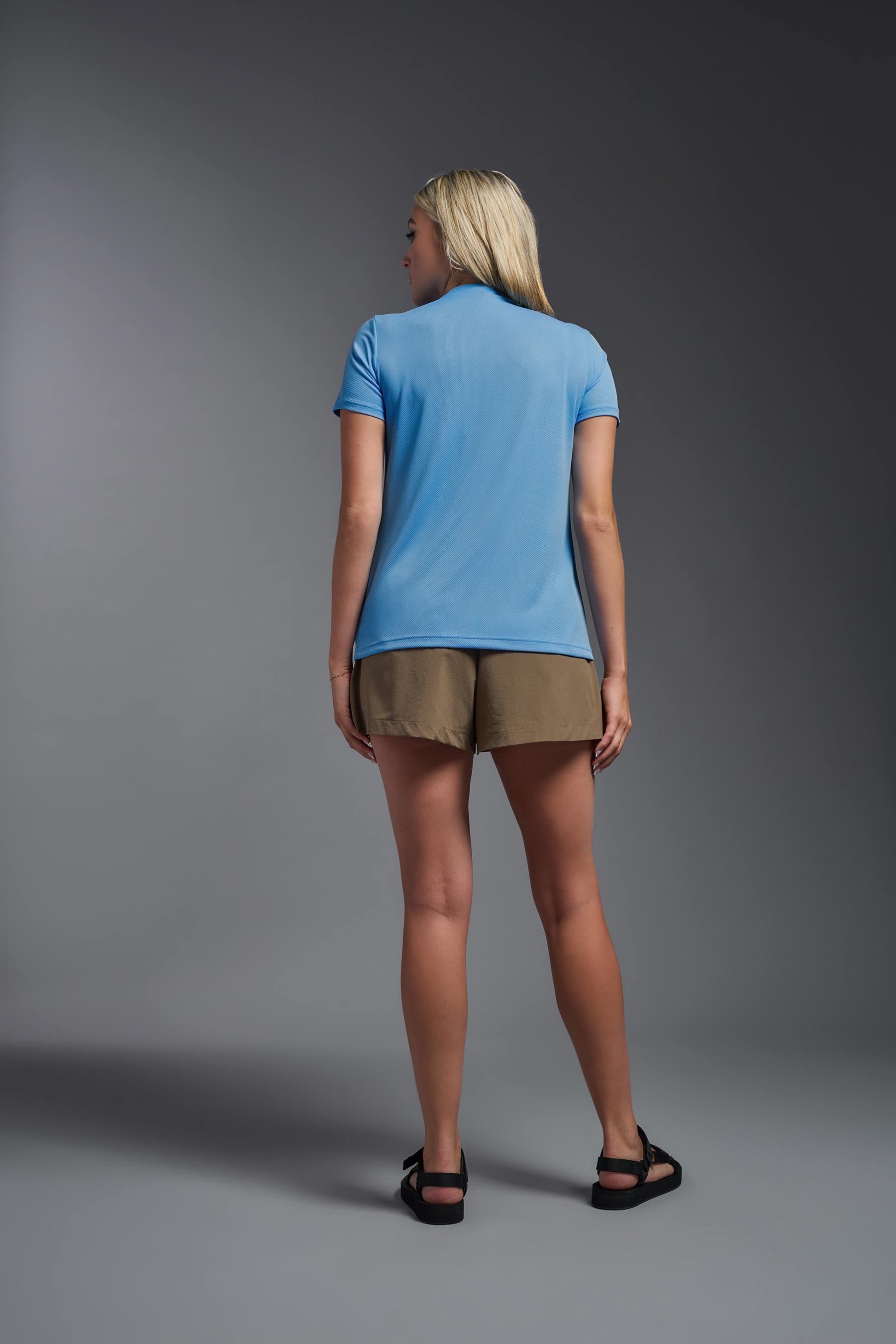 A female model wearing the women's Oxymesh V-neck Tech Tee Imported Version in the color carolina blue, made out of 100% polyester, showing the relaxed fit from a back view. This shirt is breathable, quick-drying, moisture-wicking, and Imported for a better price on bulk apparel. #carolina-blue