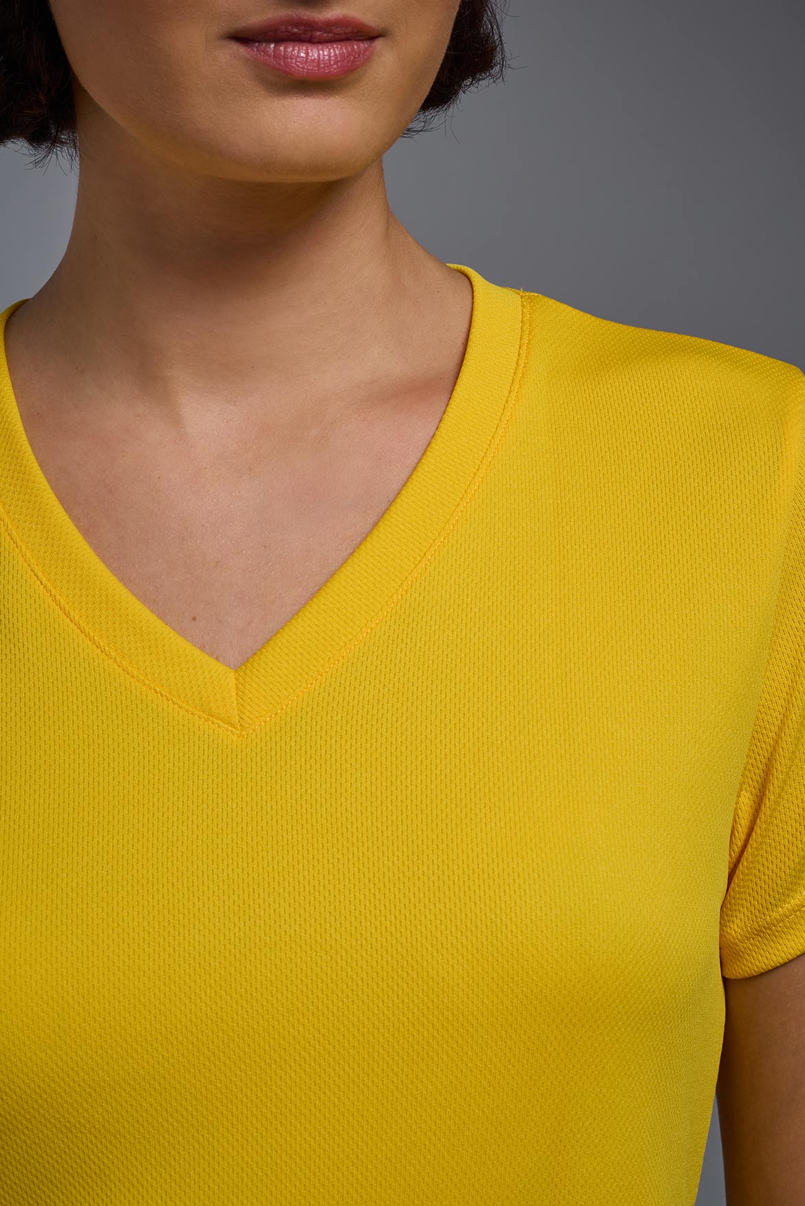 A female model wearing the women's Oxymesh V-neck Tech Tee Imported Version in the color gold, made out of 100% polyester, showing the relaxed fit from a close-up collar front view. This shirt is breathable, quick-drying, moisture-wicking, and Imported for a better price on bulk apparel. #gold