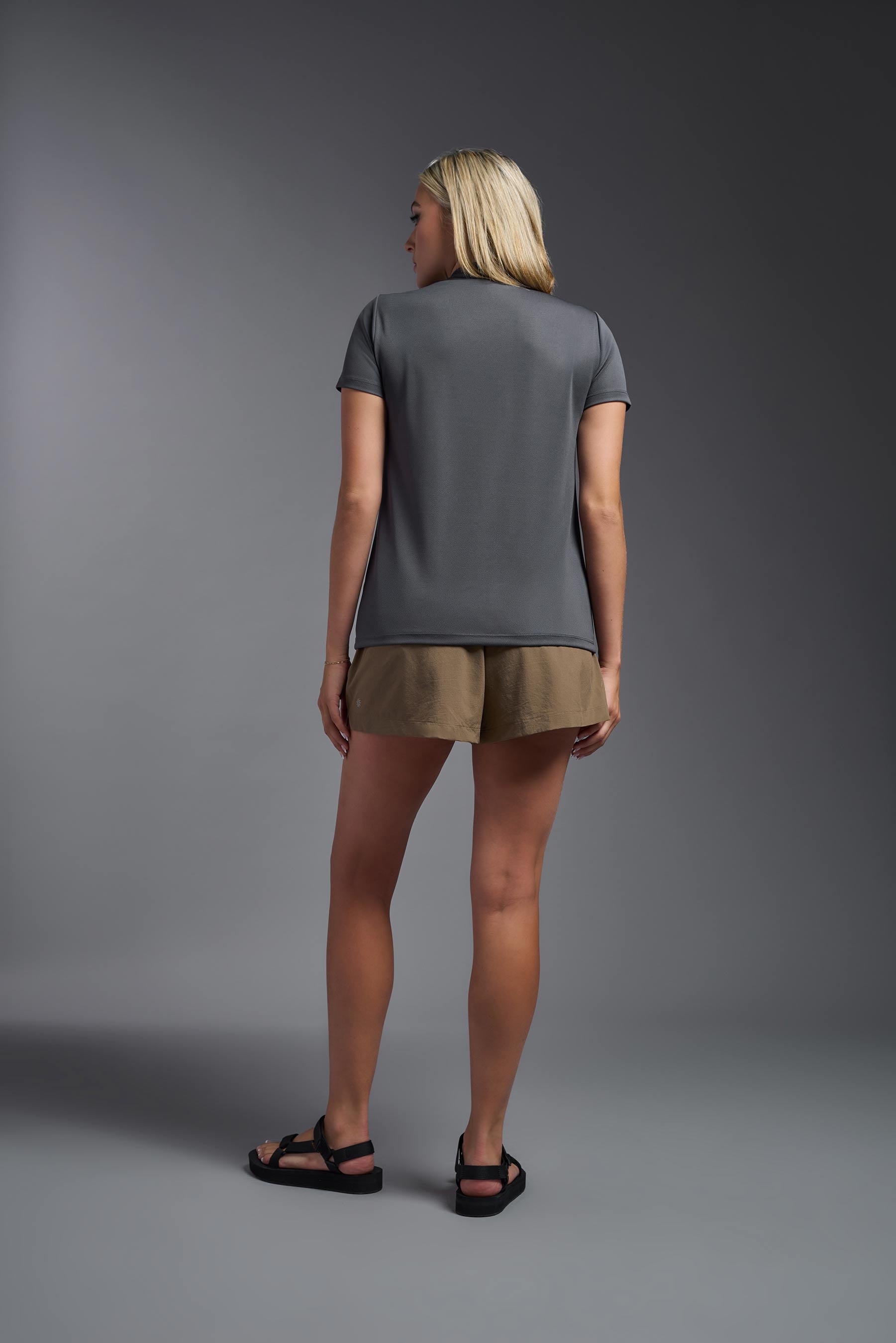 A female model wearing the women's Oxymesh V-neck Tech Tee Imported Version in the color graphite, made out of 100% polyester, showing the relaxed fit from a back view. This shirt is breathable, quick-drying, moisture-wicking, and Imported for a better price on bulk apparel. #graphite-gray