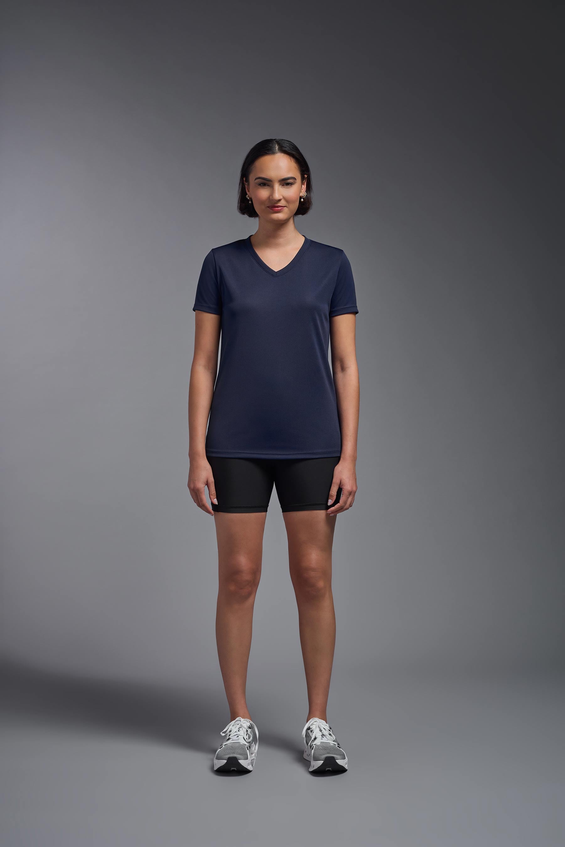 A female model wearing the women's Oxymesh V-neck Tech Tee Imported Version in the color navy, made out of 100% polyester, showing the relaxed fit from a front view. This shirt is breathable, quick-drying, moisture-wicking, and Imported for a better price on bulk apparel. #navy-blue