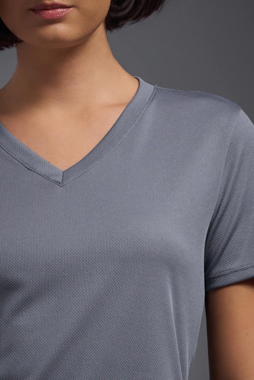 A female model wearing the women's Oxymesh V-neck Tech Tee Imported Version in the color steel gray, made out of 100% polyester, showing the relaxed fit from a close-up collar view. This shirt is breathable, quick-drying, moisture-wicking, and Imported for a better price on bulk apparel. #steel-gray