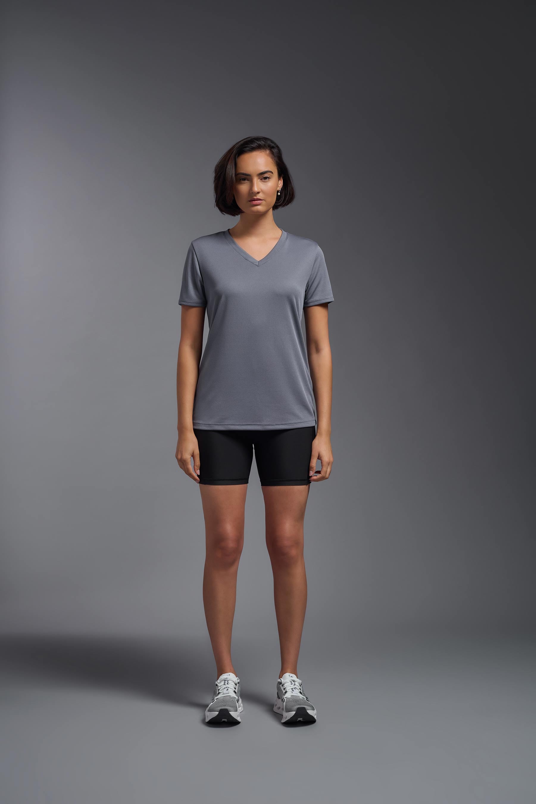 A female model wearing the women's Oxymesh V-neck Tech Tee Imported Version in the color steel gray, made out of 100% polyester, showing the relaxed fit from a front view. This shirt is breathable, quick-drying, moisture-wicking, and Imported for a better price on bulk apparel. #steel-gray