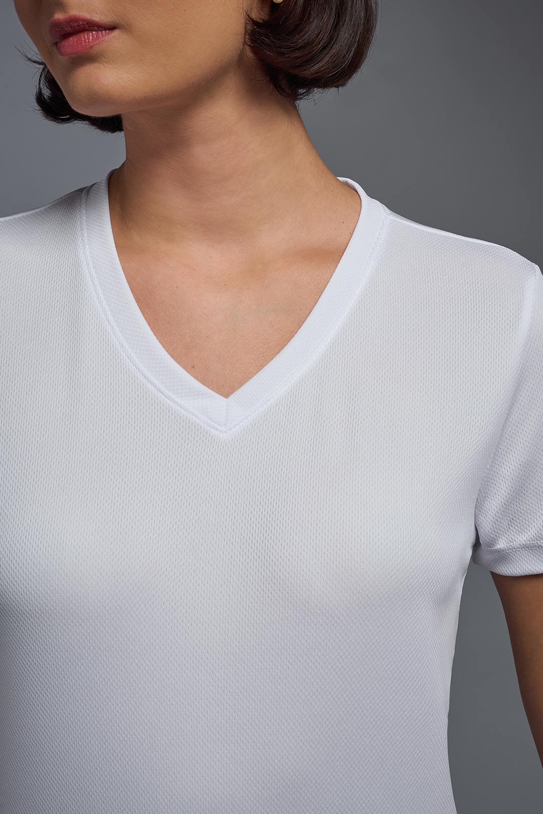 A female model wearing the women's Oxymesh V-neck Tech Tee Imported Version in the color white, made out of 100% polyester, showing the relaxed fit from a close-up collar view. This shirt is breathable, quick-drying, moisture-wicking, and Imported for a better price on bulk apparel. #white
