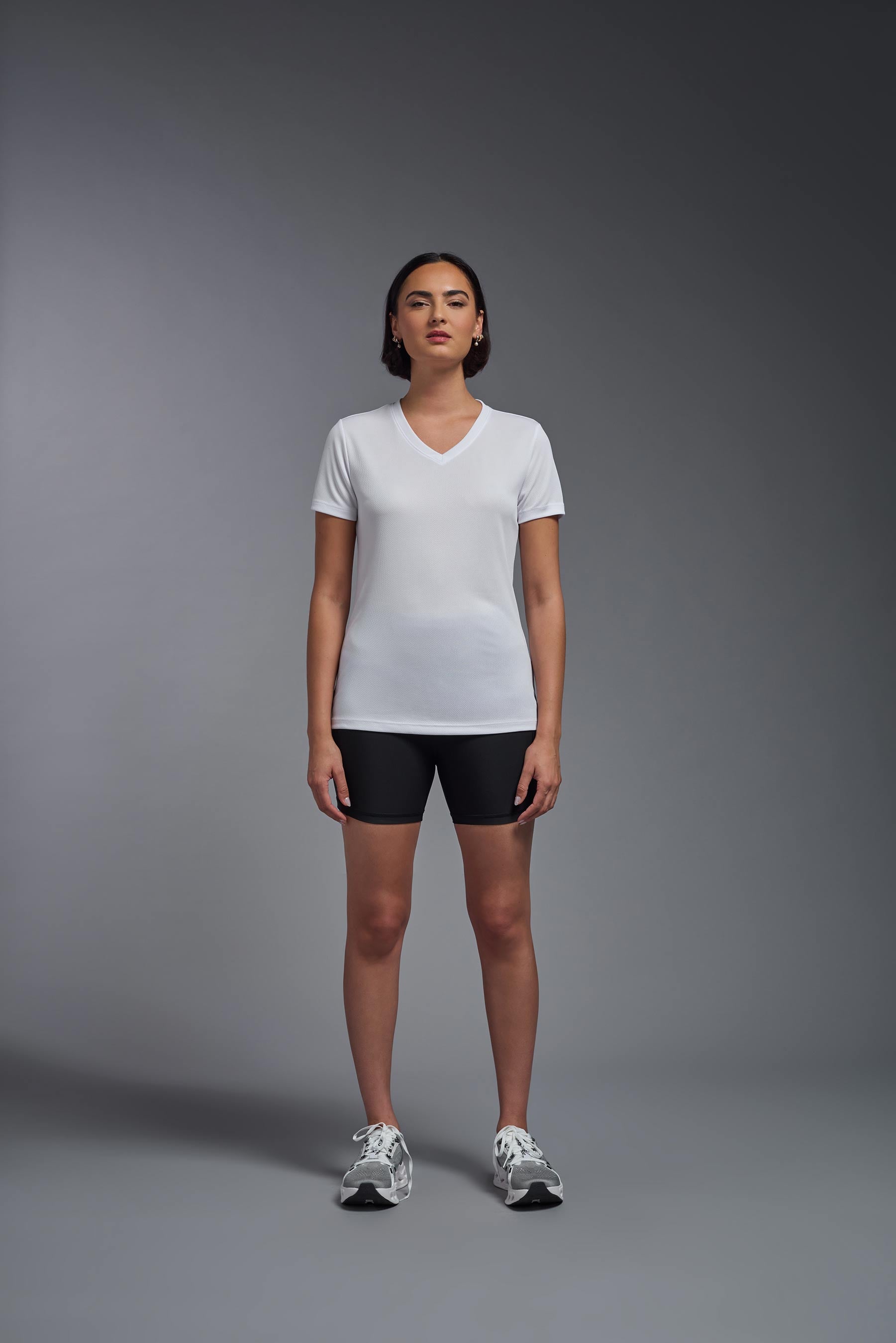 A female model wearing the women's Oxymesh V-neck Tech Tee Imported Version in the color steel-gray, made out of 100% polyester, showing the relaxed fit from a front view. This shirt is breathable, quick-drying, moisture-wicking, and Imported for a better price on bulk apparel. #white