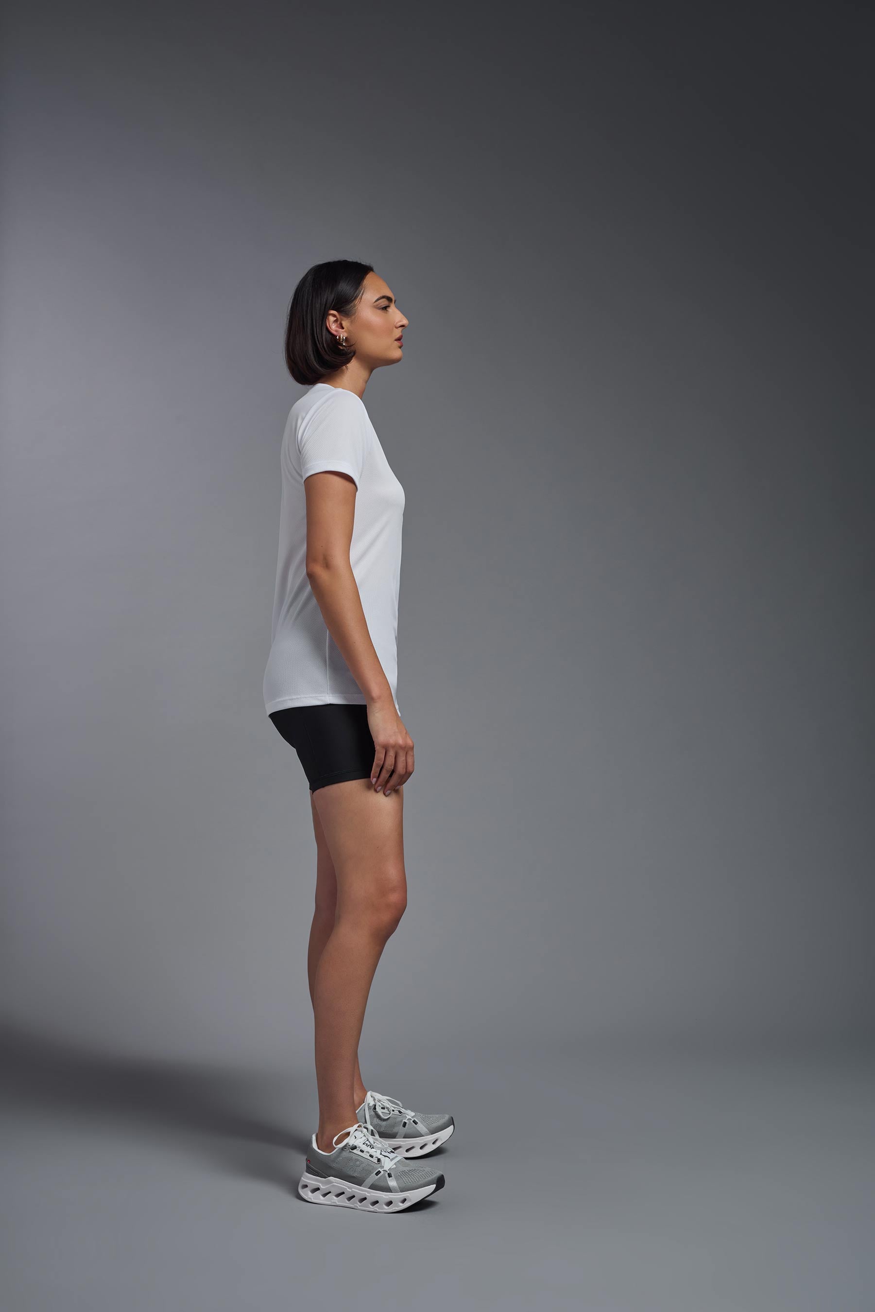 A female model wearing the women's Oxymesh V-neck Tech Tee Imported Version in the color white, made out of 100% polyester, showing the relaxed fit from a side view. This shirt is breathable, quick-drying, moisture-wicking, and Imported for a better price on bulk apparel. #white