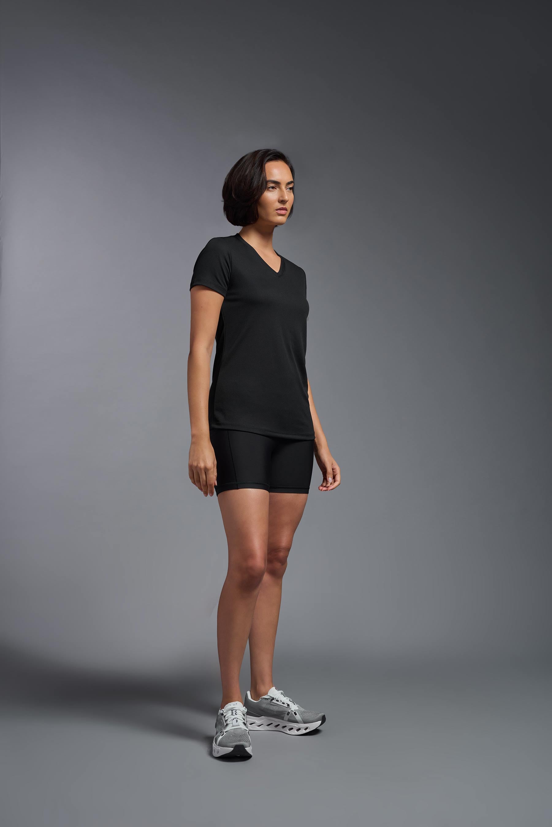 A female model wearing the women's Oxymesh V-neck Tech Tee in the color black, made out of 100% polyester, showing the relaxed fit from a side view. This shirt is breathable, wicks away moisture, quick-dries, and is made in the USA. #black