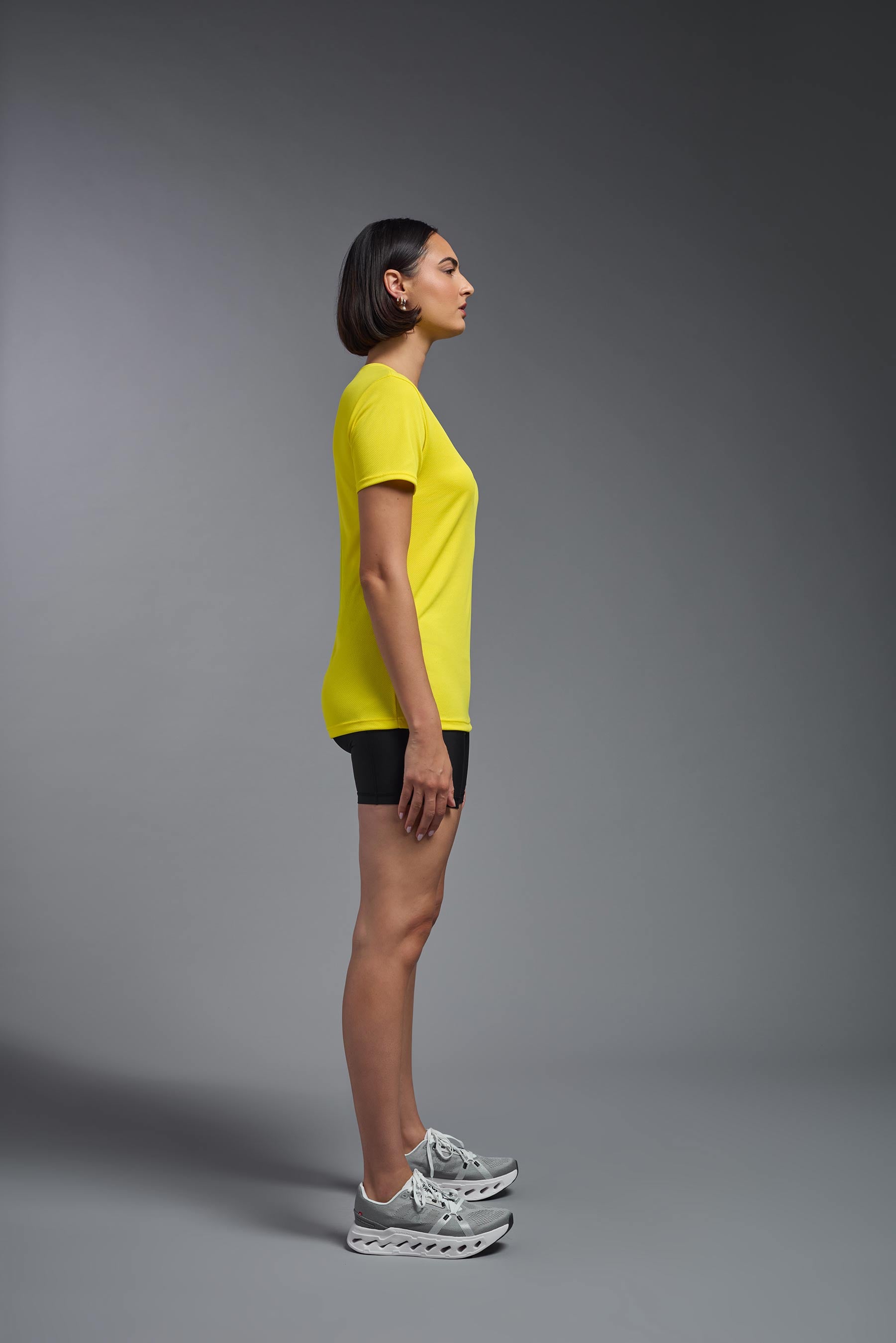 A female model wearing the women's Oxymesh V-neck Tech Tee in the color bright yellow, made out of 100% polyester, showing the relaxed fit from a side view. This shirt is breathable, wicks away moisture, quick-dries, and is made in the USA. #bright-yellow