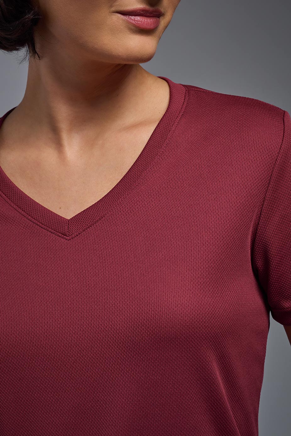 A female model wearing the women's Oxymesh V-neck Tech Tee in the color cardinal, made out of 100% polyester, showing the relaxed fit from a close-up collar view. This shirt is breathable, wicks away moisture, quick-dries, and is made in the USA. #cardinal-red