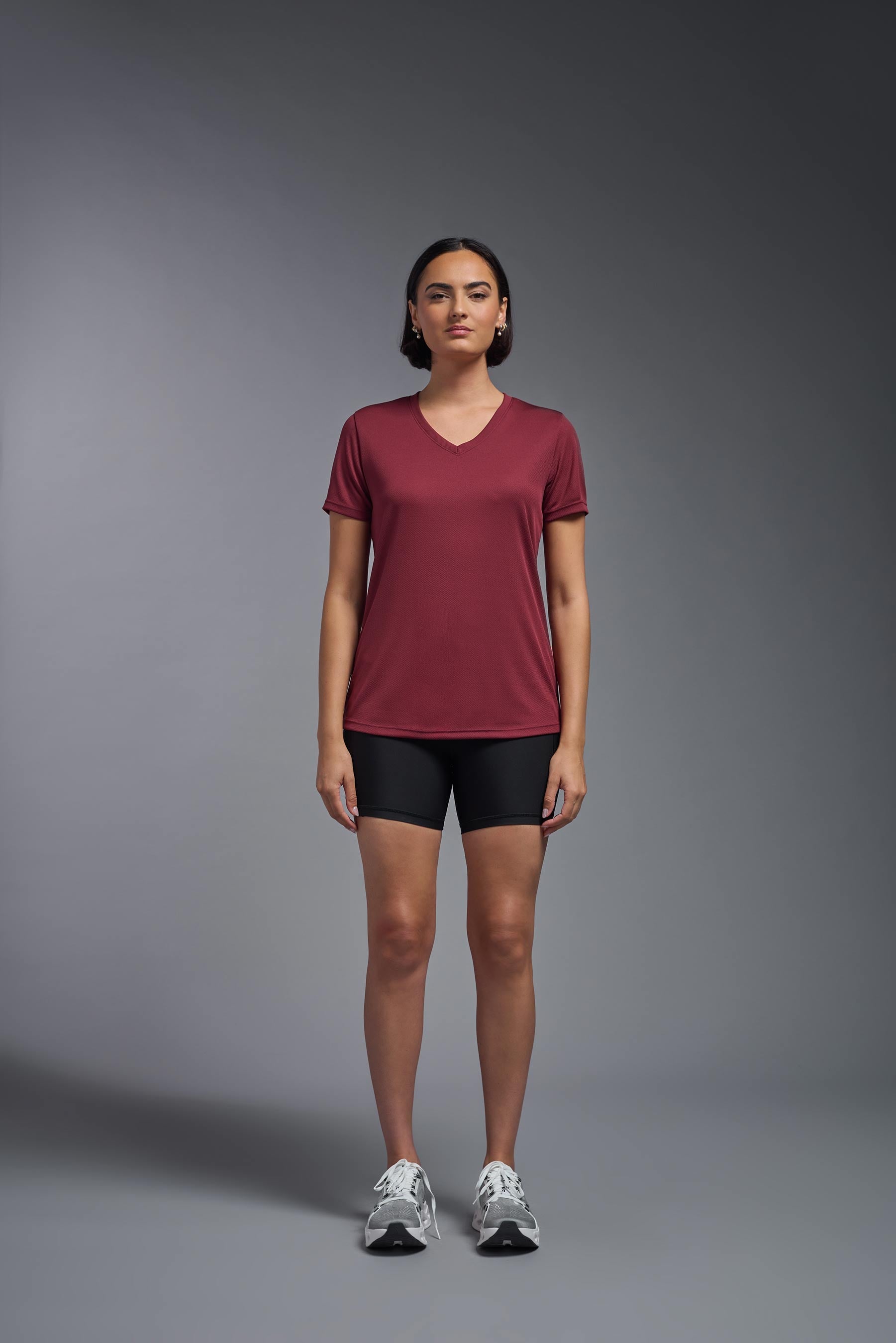 A female model wearing the women's Oxymesh V-neck Tech Tee in the color cardinal, made out of 100% polyester, showing the relaxed fit from a front view. This shirt is breathable, wicks away moisture, quick-dries, and is made in the USA. #cardinal-red