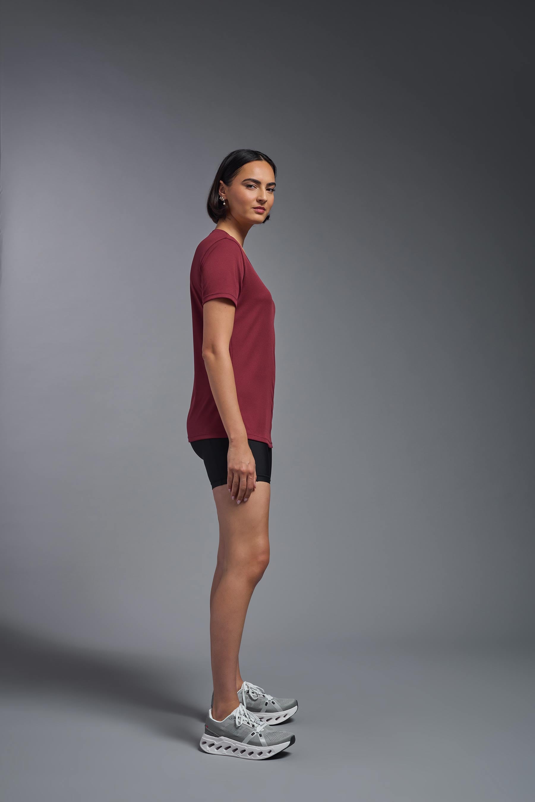 A female model wearing the women's Oxymesh V-neck Tech Tee in the color cardinal, made out of 100% polyester, showing the relaxed fit from a side view. This shirt is breathable, wicks away moisture, quick-dries, and is made in the USA. #cardinal-red