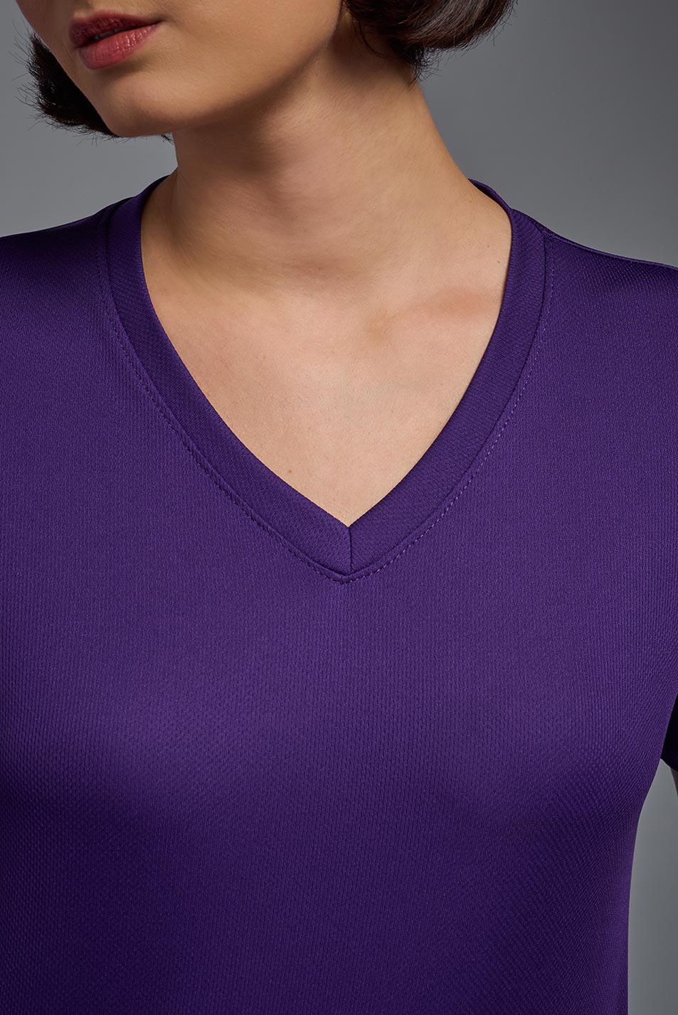 A female model wearing the women's Oxymesh V-neck Tech Tee in the color dark purple, made out of 100% polyester, showing the relaxed fit from a closeup collar view. This shirt is breathable, wicks away moisture, quick-dries, and is made in the USA. #dark-purple