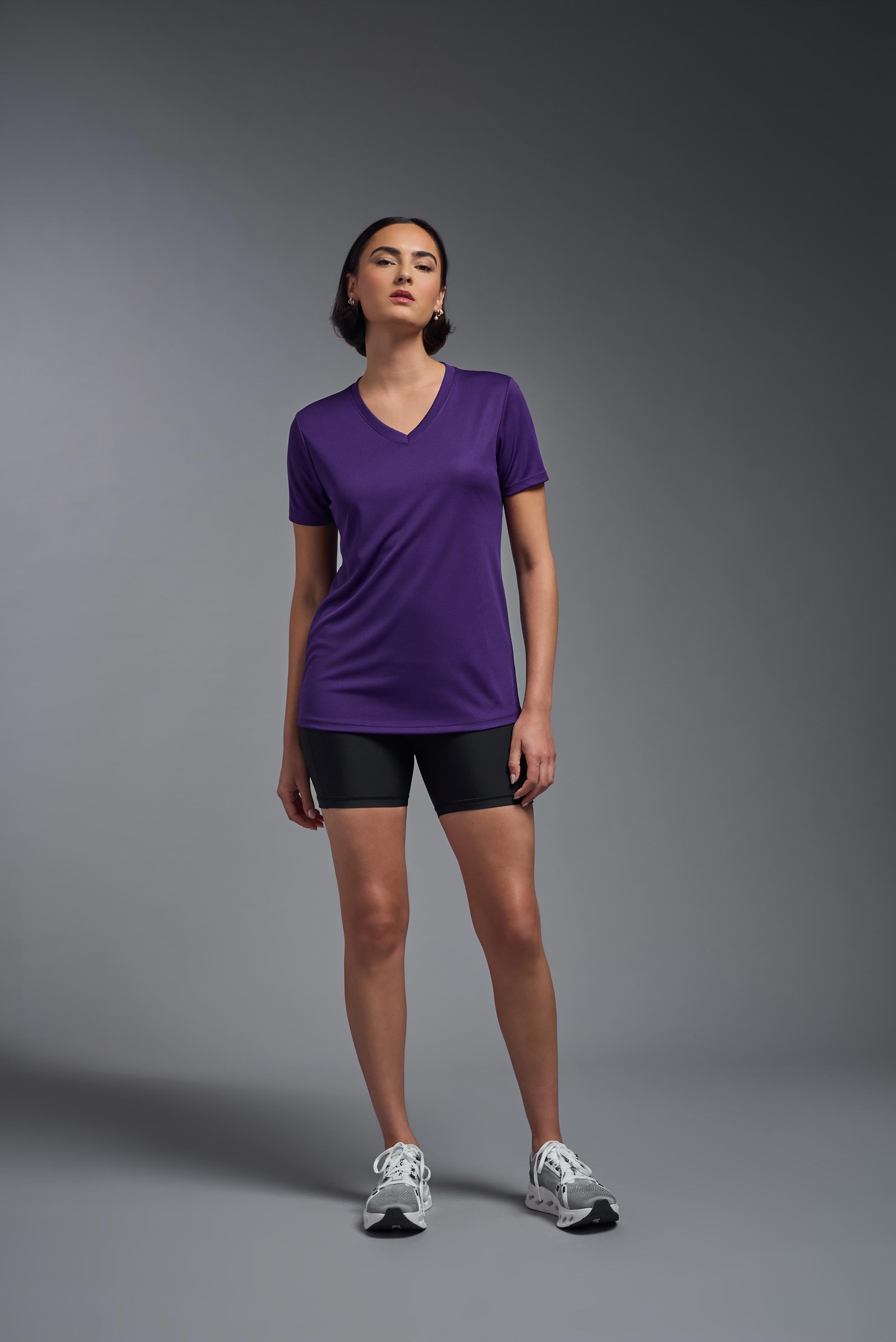 A female model wearing the women's Oxymesh V-neck Tech Tee in the color dark purple, made out of 100% polyester, showing the relaxed fit from a front view. This shirt is breathable, wicks away moisture, quick-dries, and is made in the USA. #dark-purple