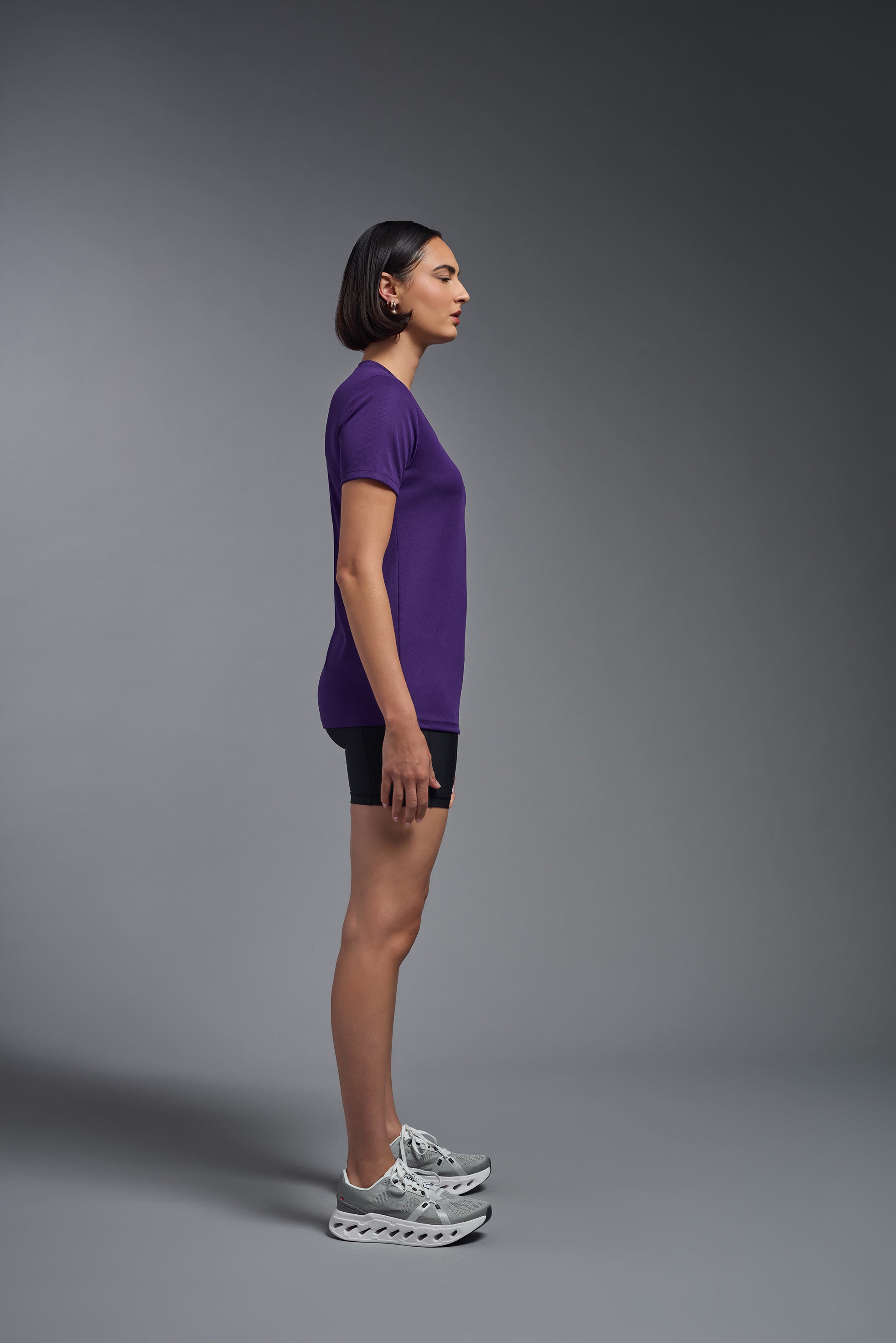 A female model wearing the women's Oxymesh V-neck Tech Tee in the color dark purple, made out of 100% polyester, showing the relaxed fit from a side view. This shirt is breathable, wicks away moisture, quick-dries, and is made in the USA. #dark-purple