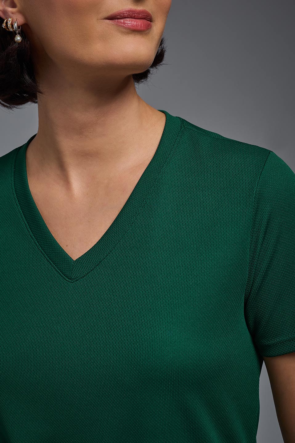A female model wearing the women's Oxymesh V-neck Tech Tee in the color forest green, made out of 100% polyester, showing the relaxed fit from a collar close-up view. This shirt is breathable, wicks away moisture, quick-dries, and is made in the USA. #forest-green