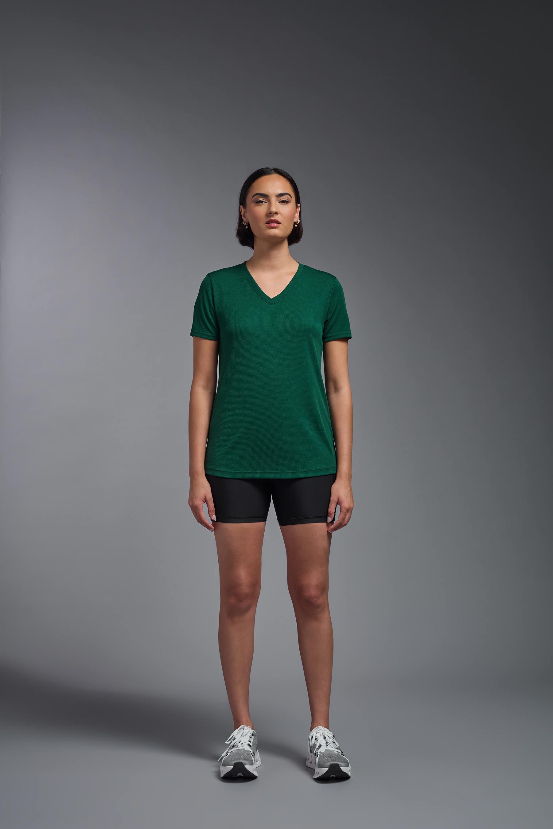 A female model wearing the women's Oxymesh V-neck Tech Tee in the color forest green, made out of 100% polyester, showing the relaxed fit from a front view. This shirt is breathable, wicks away moisture, quick-dries, and is made in the USA. #forest-green