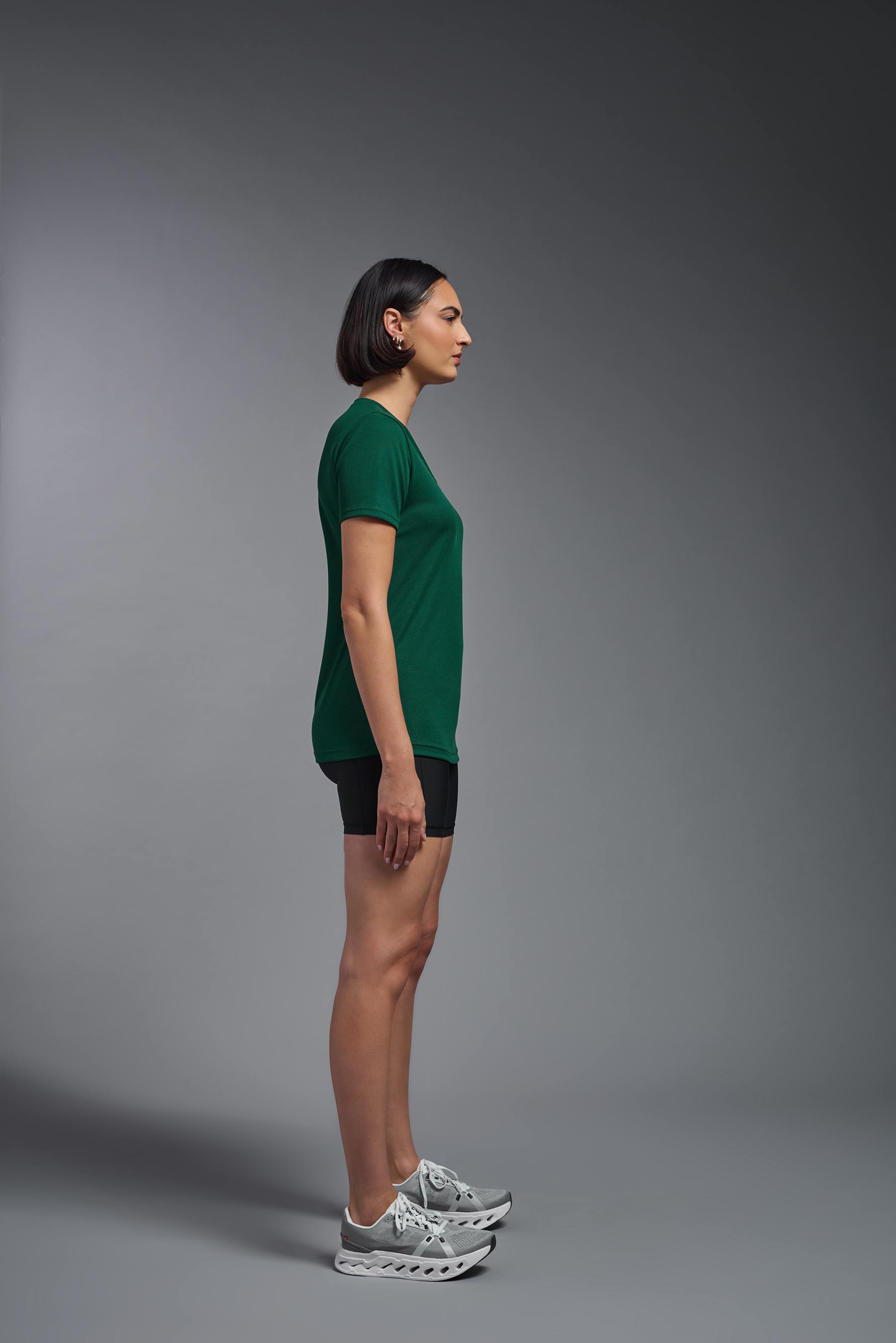 A female model wearing the women's Oxymesh V-neck Tech Tee in the color forest green, made out of 100% polyester, showing the relaxed fit from a side view. This shirt is breathable, wicks away moisture, quick-dries, and is made in the USA. #forest-green