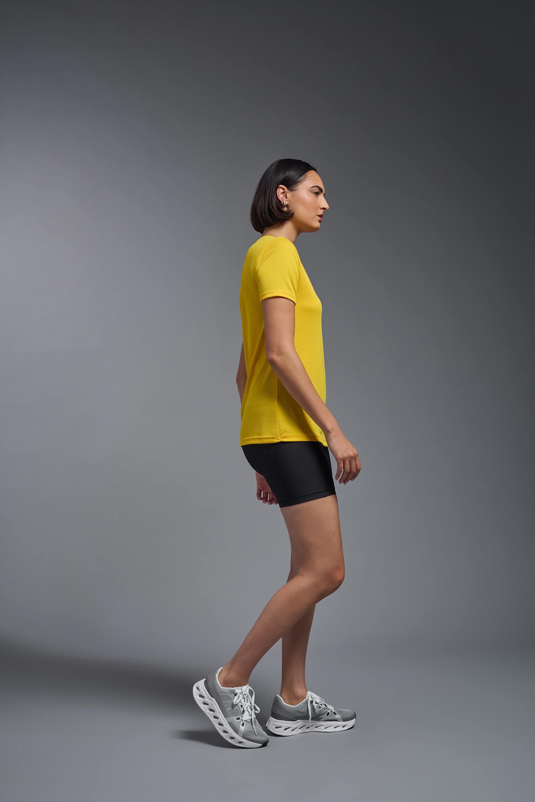 A female model wearing the women's Oxymesh V-neck Tech Tee in the color gold, made out of 100% polyester, showing the relaxed fit from a side view. This shirt is breathable, wicks away moisture, quick-dries, and is made in the USA. #gold