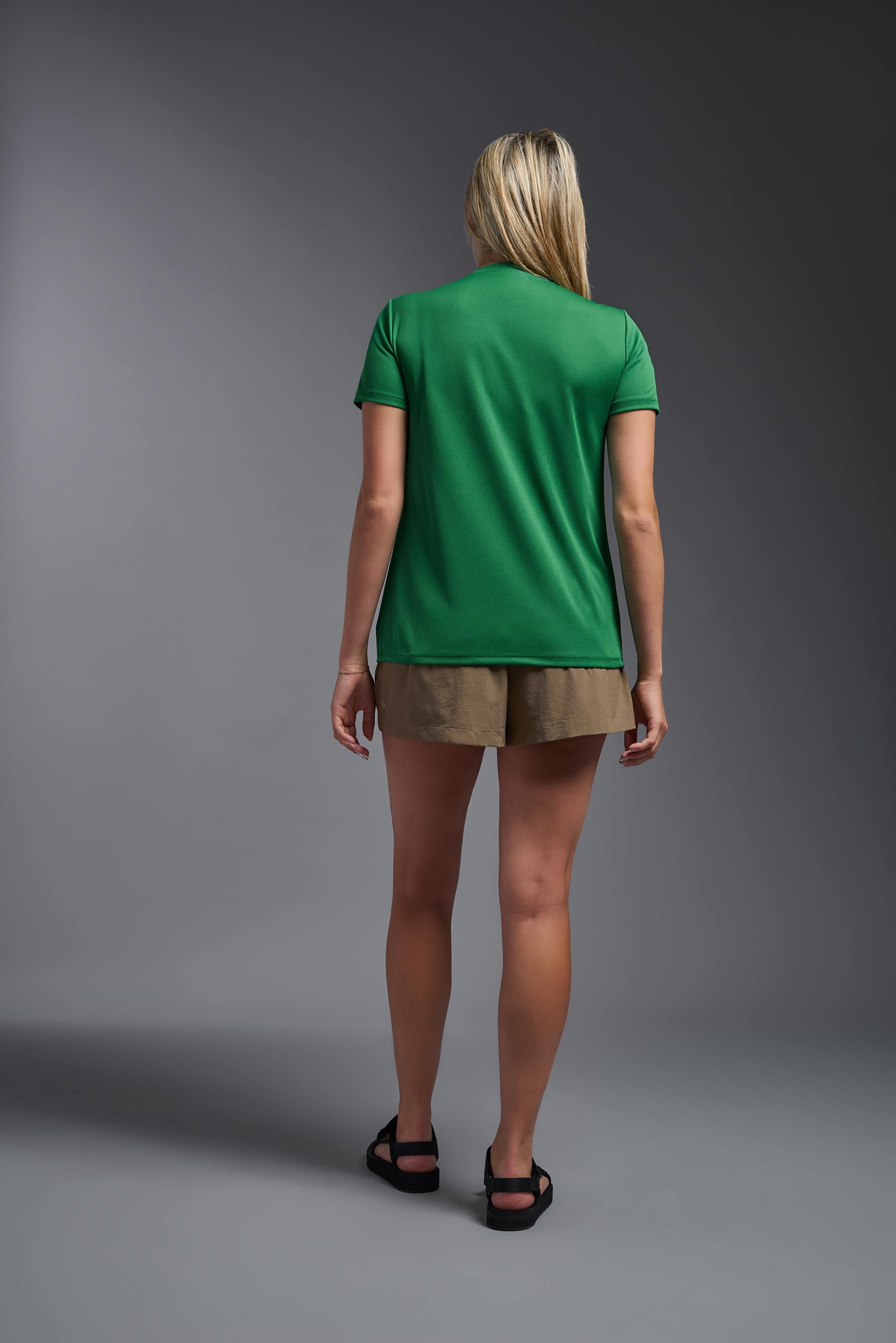 A female model wearing the women's Oxymesh V-neck Tech Tee in the color kelly green, made out of 100% polyester, showing the relaxed fit from a back view. This shirt is breathable, wicks away moisture, quick-dries, and is made in the USA. #kelly-green