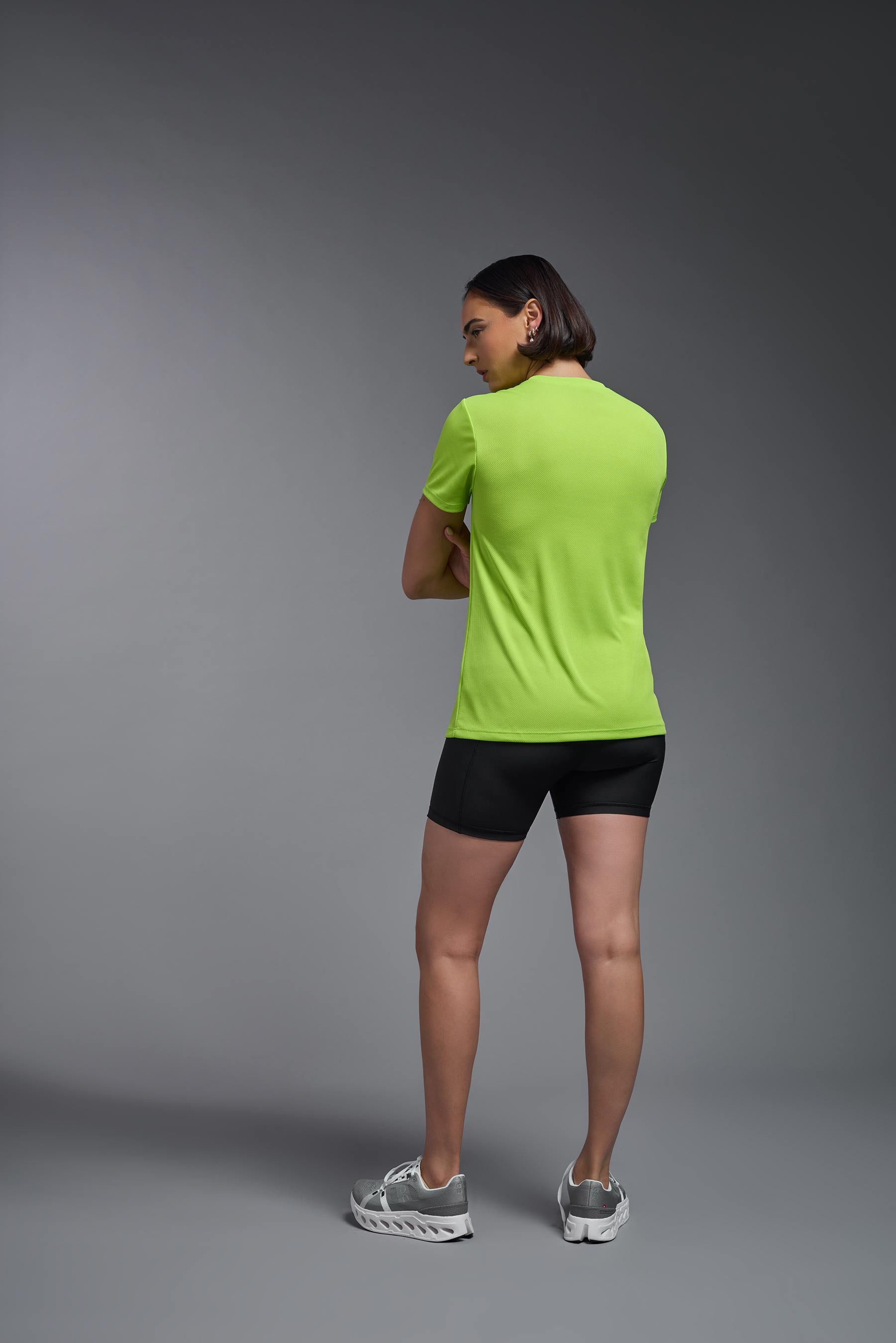 A female model wearing the women's Oxymesh V-neck Tech Tee in the color key lime, made out of 100% polyester, showing the relaxed fit from a back view. This shirt is breathable, wicks away moisture, quick-dries, and is made in the USA. #key-lime
