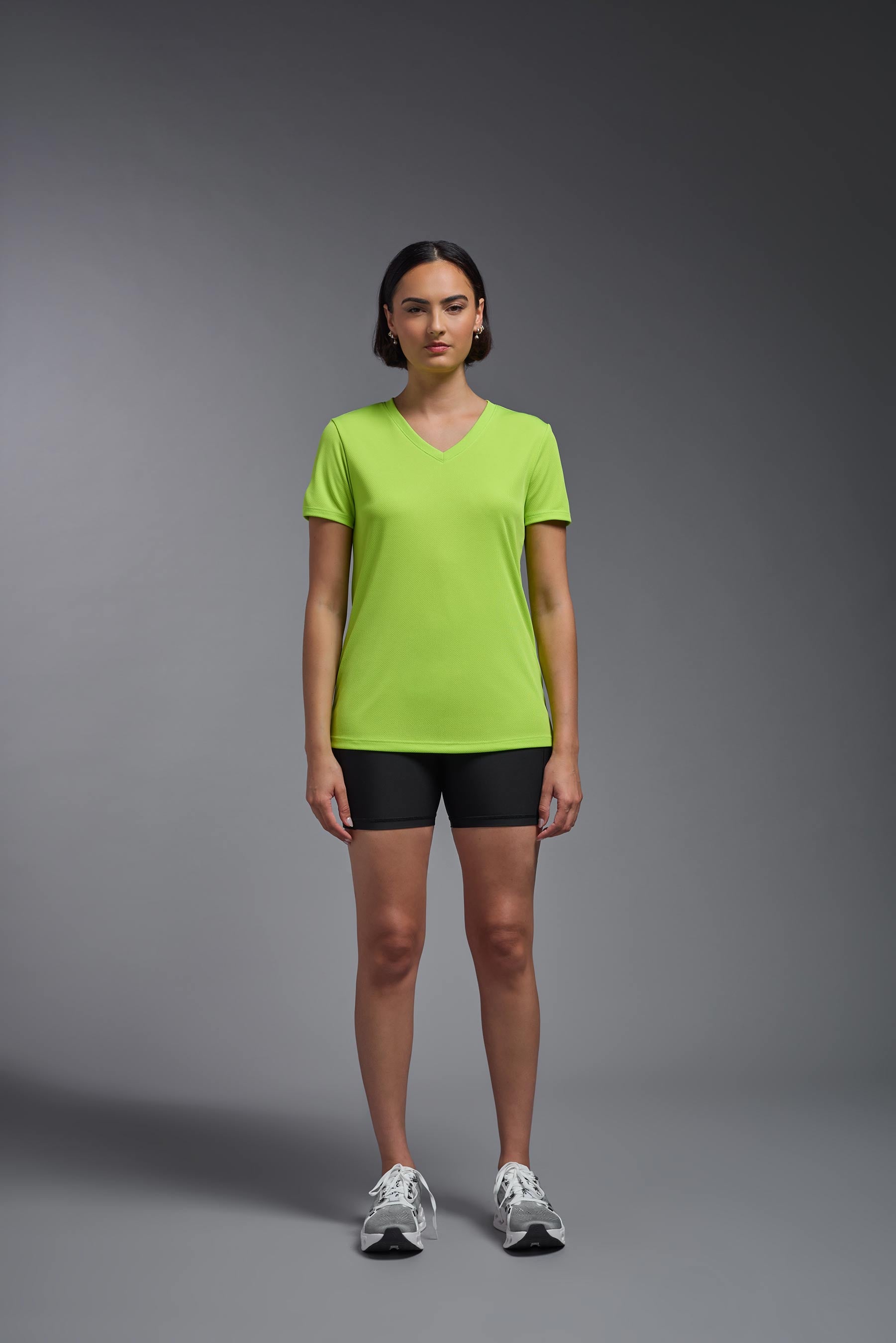A female model wearing the women's Oxymesh V-neck Tech Tee in the color key lime, made out of 100% polyester, showing the relaxed fit from a front view. This shirt is breathable, wicks away moisture, quick-dries, and is made in the USA. #key-lime