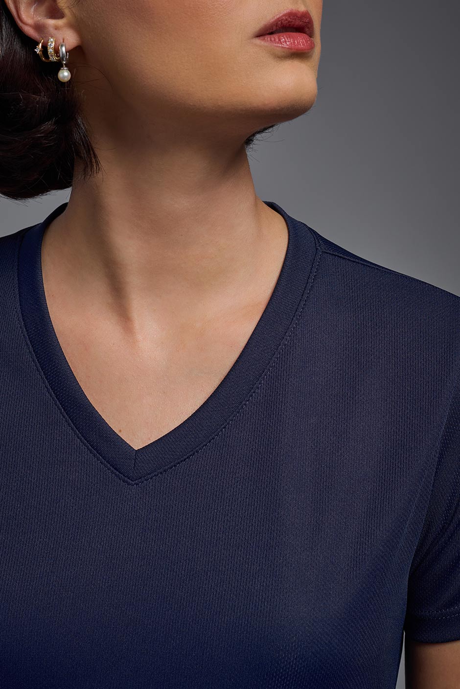 A female model wearing the women's Oxymesh V-neck Tech Tee in the color navy, made out of 100% polyester, showing the relaxed fit from a close-up collar view. This shirt is breathable, wicks away moisture, quick-dries, and is made in the USA. #navy-blue