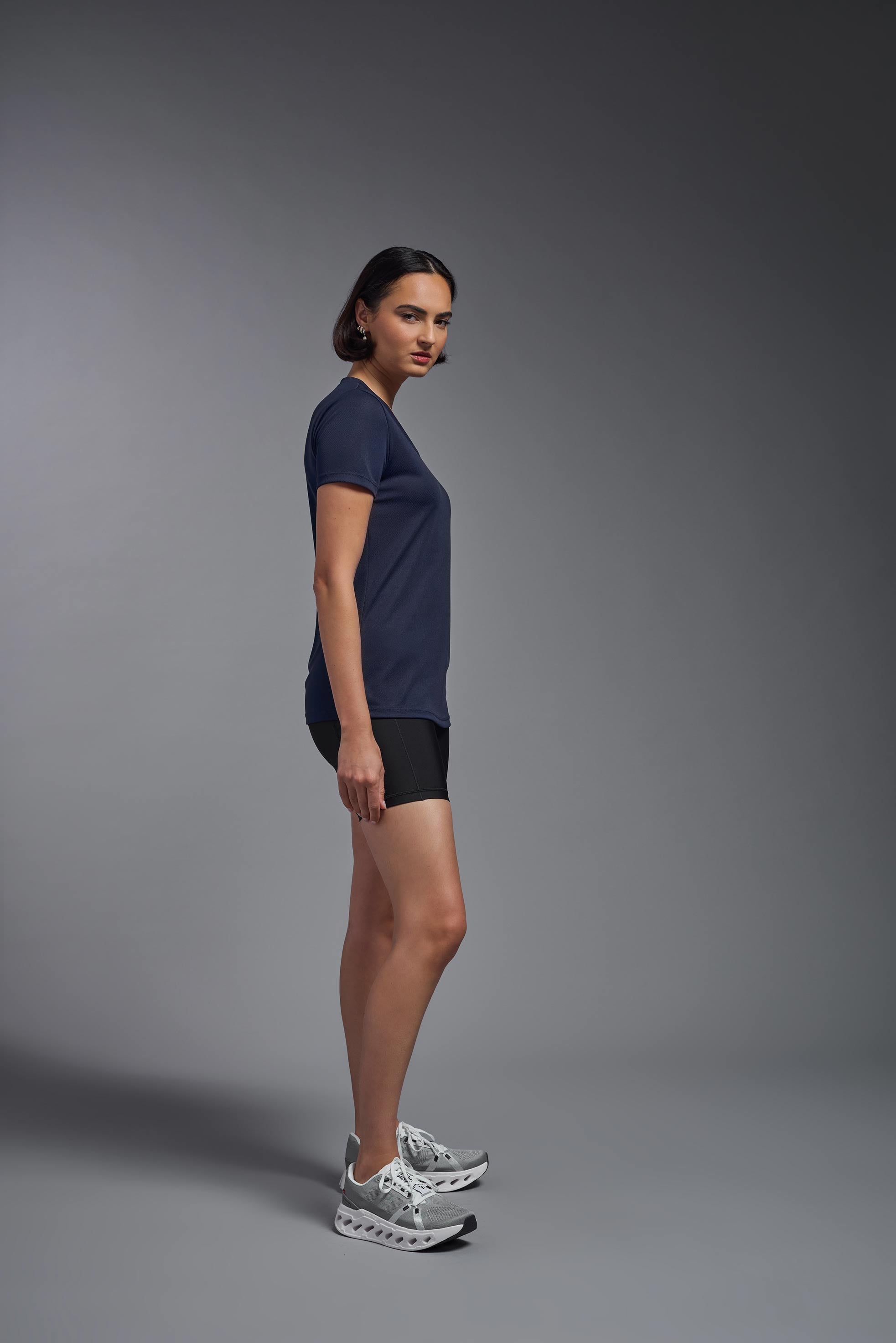A female model wearing the women's Oxymesh V-neck Tech Tee in the color navy, made out of 100% polyester, showing the relaxed fit from a side view. This shirt is breathable, wicks away moisture, quick-dries, and is made in the USA. #navy-blue