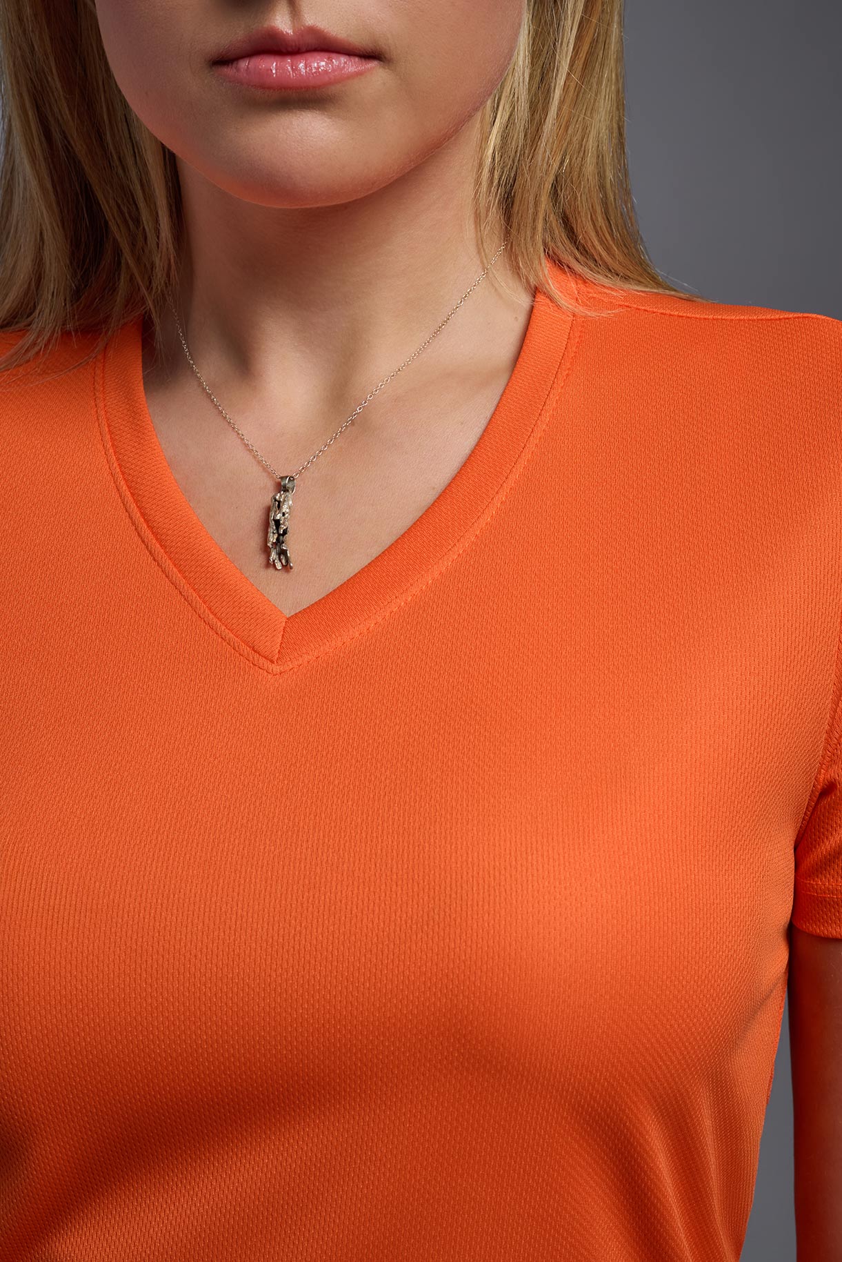 A female model wearing the women's Oxymesh V-neck Tech Tee in the color orange, made out of 100% polyester, showing the relaxed fit from a close-up collar view. This shirt is breathable, wicks away moisture, quick-dries, and is made in the USA. #orange