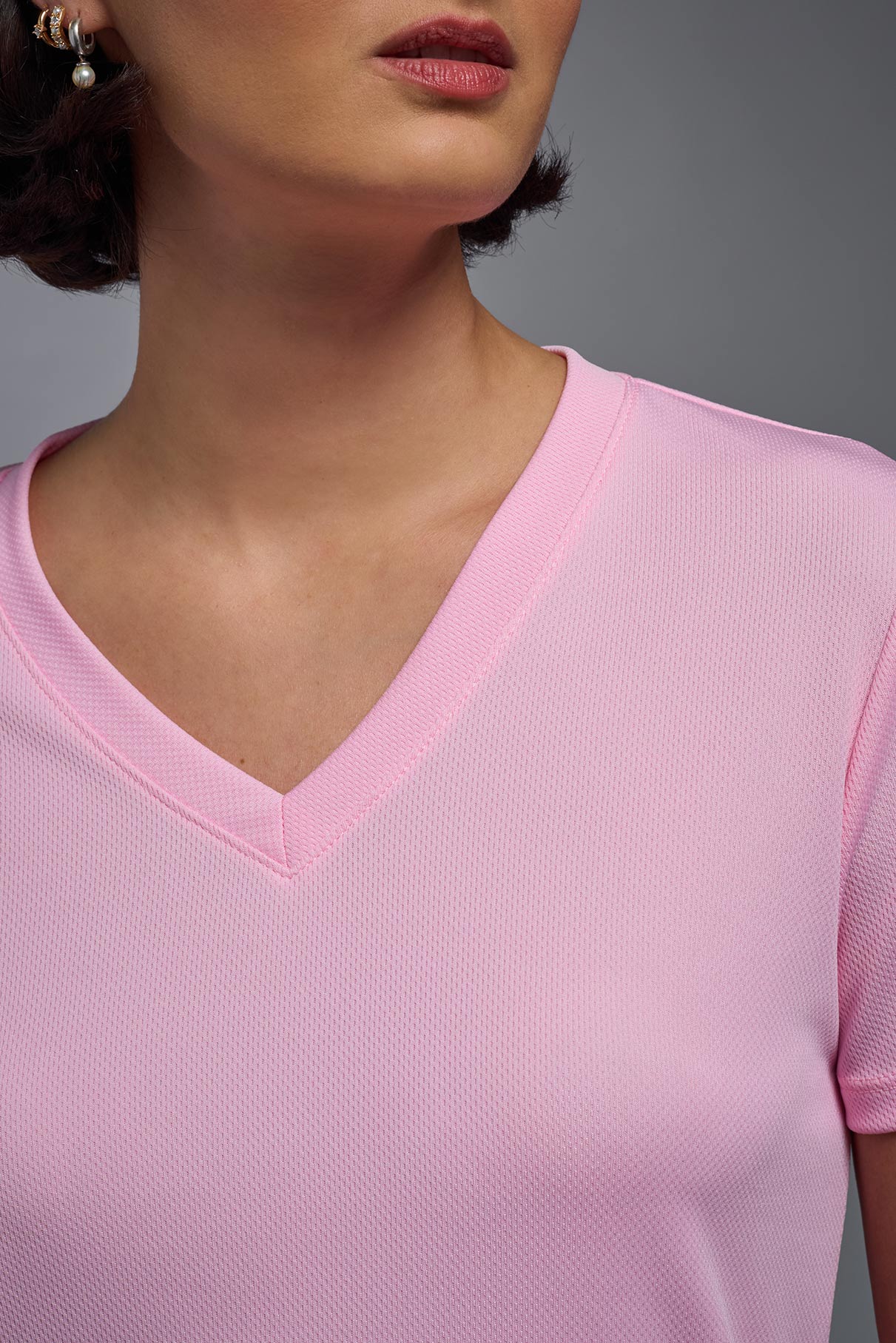 A female model wearing the women's Oxymesh V-neck Tech Tee in the color pink, made out of 100% polyester, showing the relaxed fit from a close-up collar view. This shirt is breathable, wicks away moisture, quick-dries, and is made in the USA. #pink